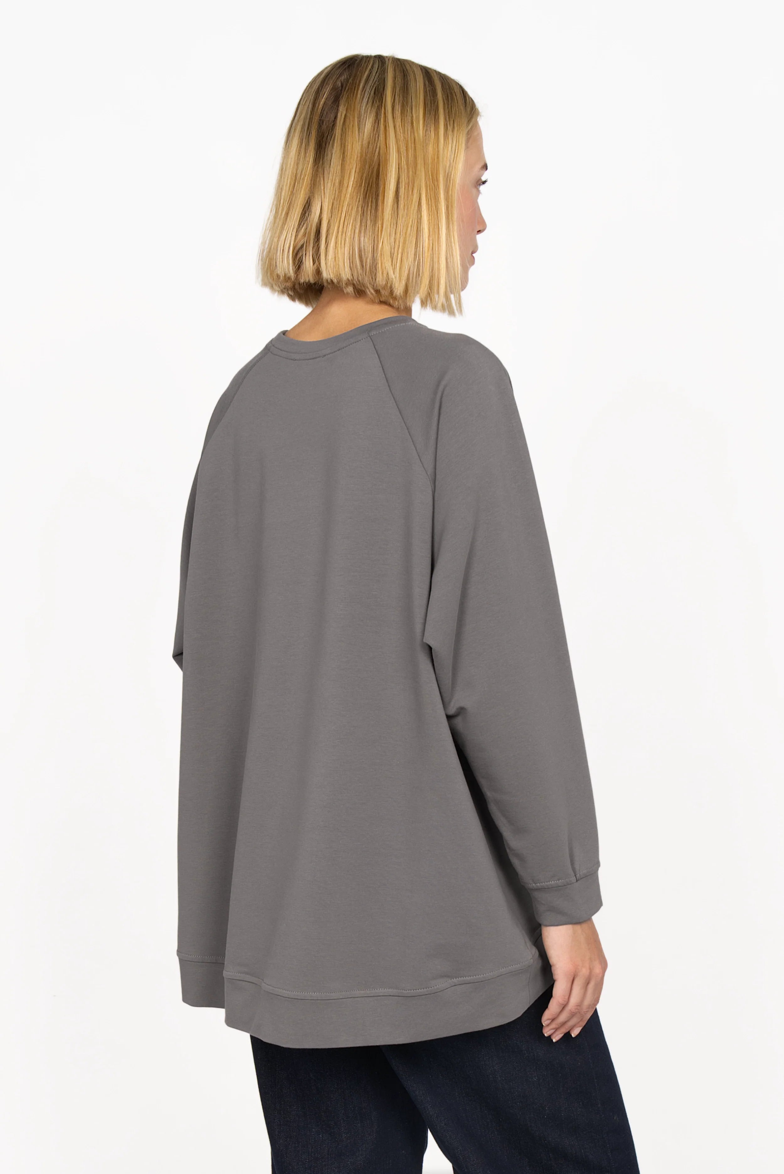 Back view of a model wearing a grey GRACEY.K Sweater with an oversized fit and longer A-line hem.
