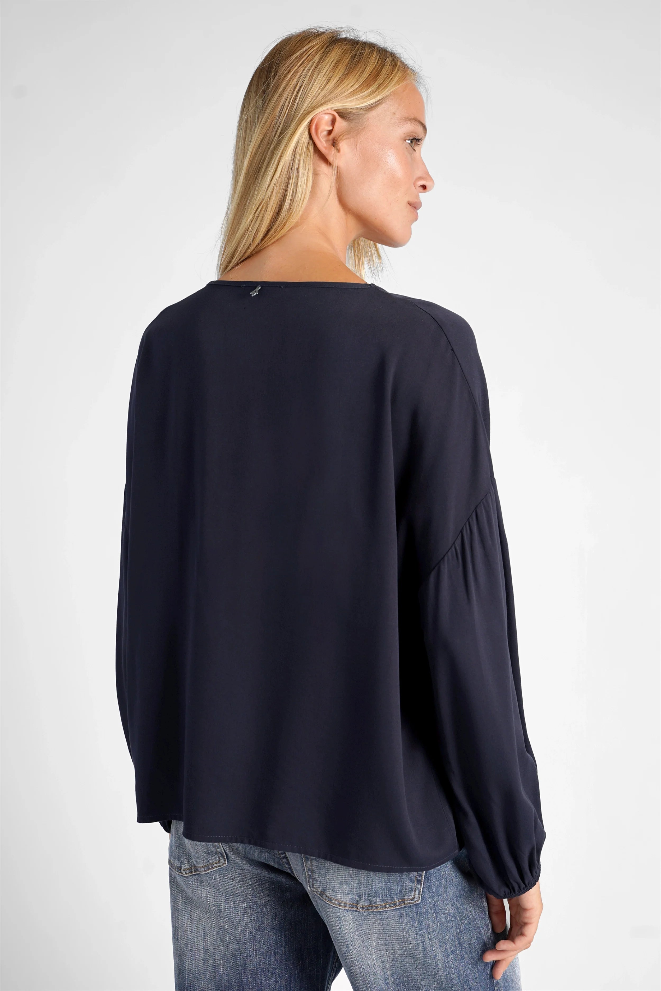 Dunkelblaue GRETA.K V-Neck Bluse aus leichter Viskose mit Ballonärmeln, locker fallend, Rücklänge ca. 60 cm, getragen von Modell in Größe S