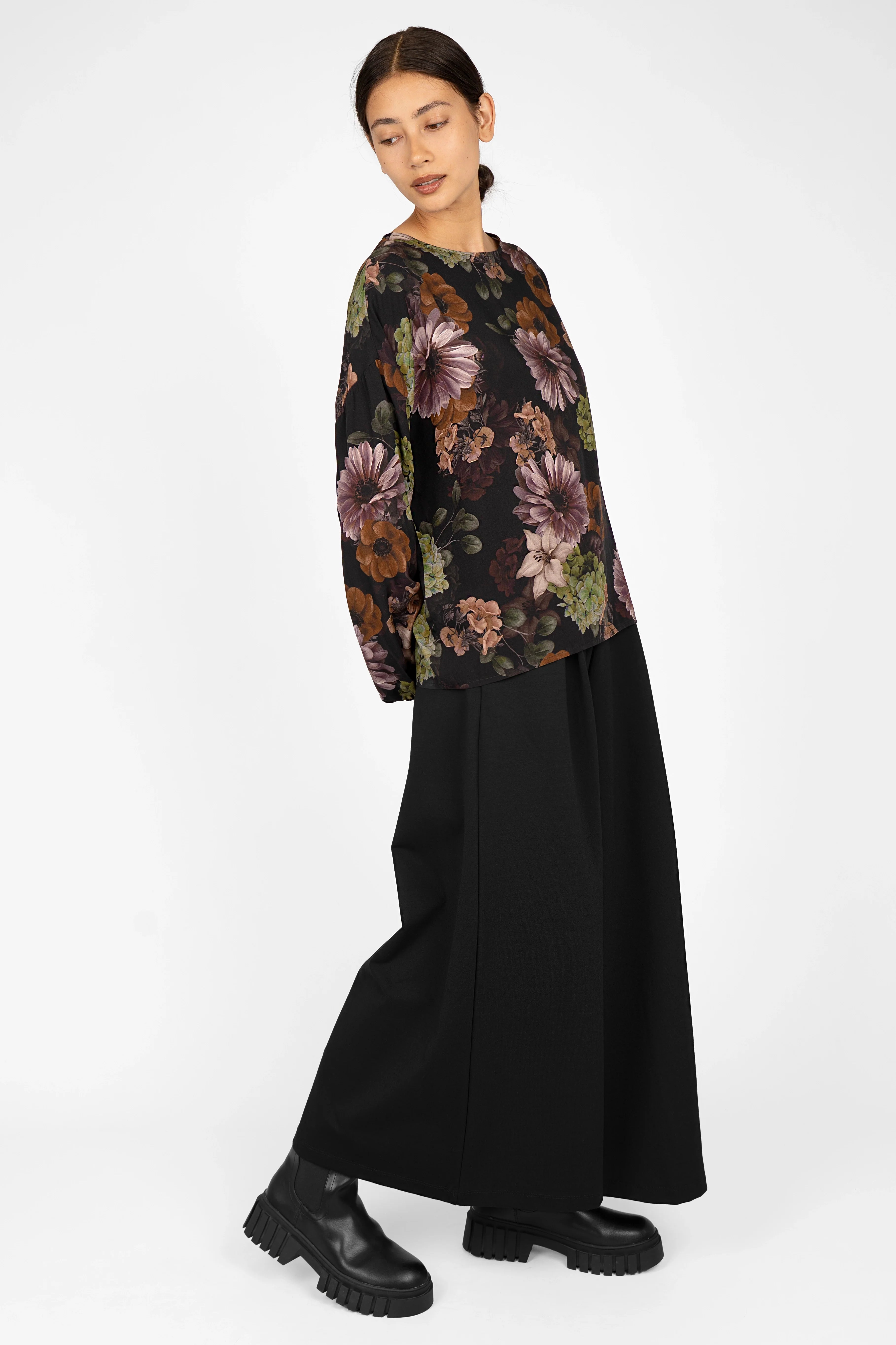 Woman wearing GRETA.K Bluse with allover floral print, round neck, and balloon sleeves paired with black skirt and boots