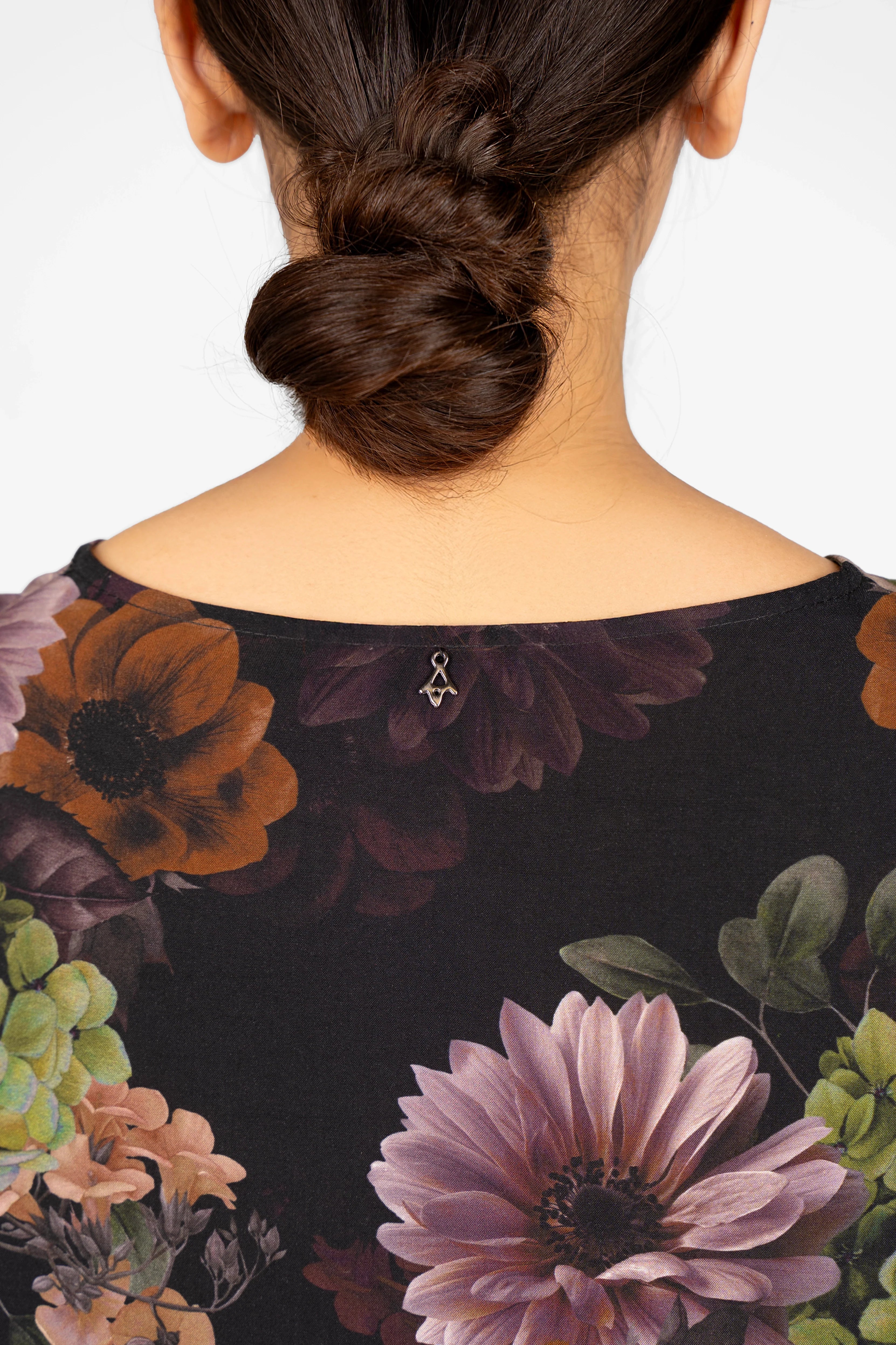 Back view of GRETA.K Bluse with dark floral allover print and round neckline on model with bun hairstyle.