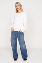 Damen trägt weiße GRETA.K Bluse mit Rundhalsausschnitt, überschnittenen Schultern und elastischen Ärmeln kombiniert mit blauen Jeans