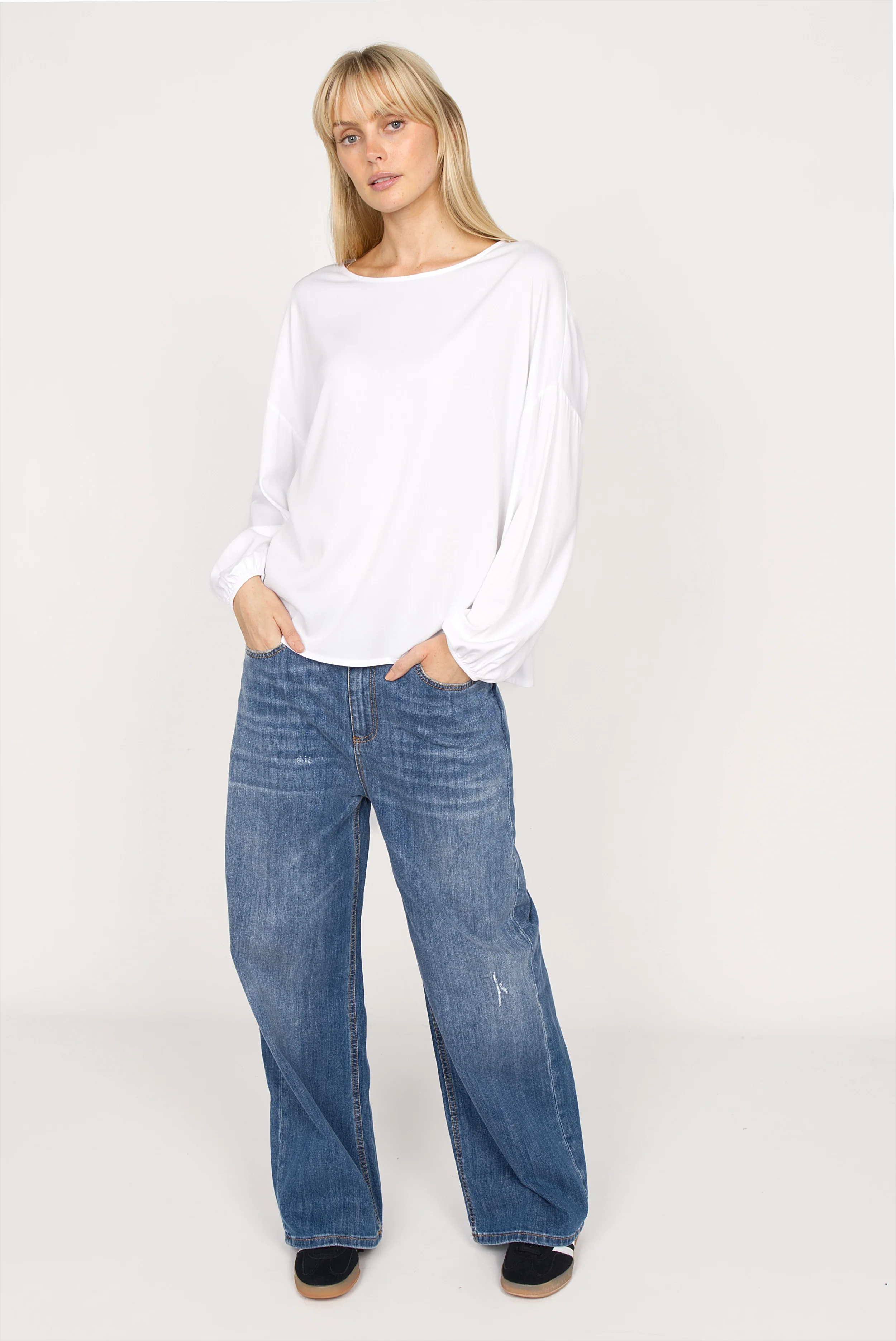 Damen trägt weiße GRETA.K Bluse mit Rundhalsausschnitt, überschnittenen Schultern und elastischen Ärmeln kombiniert mit blauen Jeans