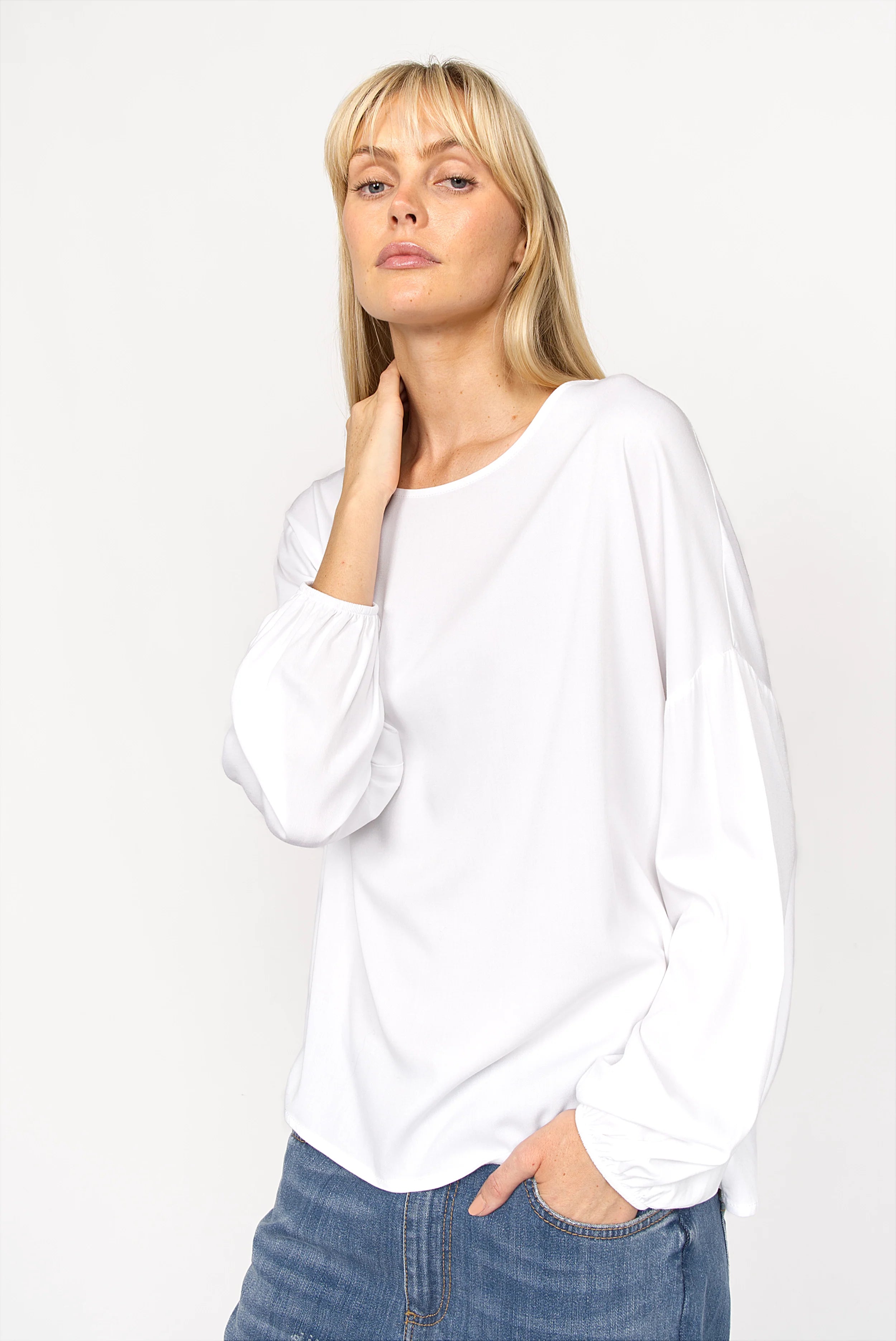 Frau trägt weiße GRETA.K Bluse aus locker geschnittener Twill Viskose mit Rundhalsausschnitt und langen Ärmeln mit elastischen Abschlüssen.