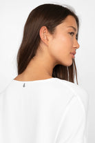Frau trägt weiße GRETA.K V-Neck Bluse mit überschnittenen Schultern und elastischen Ärmelabschlüssen, seitliche Nahaufnahme