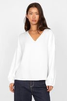 Damenmodel trägt weiße GRETA.K V-Neck Bluse mit V-Ausschnitt und langen Ärmeln in relaxed Fit