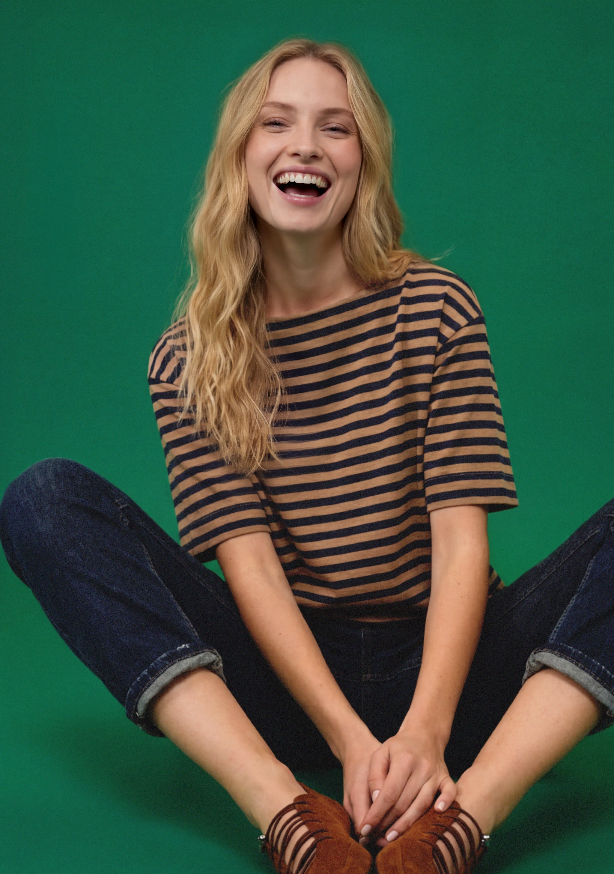 Lachendes Model im gestreiften Shirt und dunkler Jeans vor grünem Hintergrund.