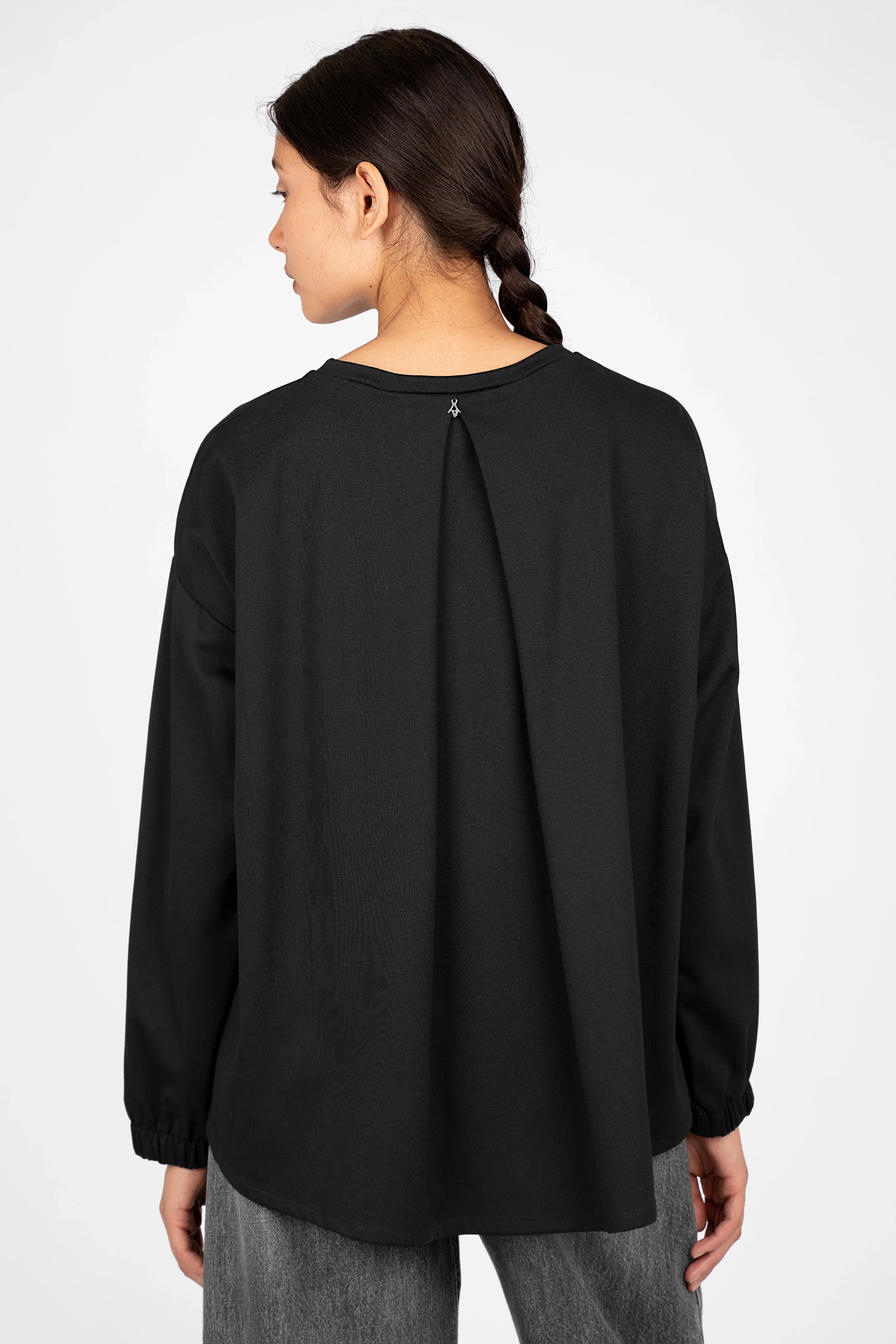Back view of a woman wearing a black HAGLA Shirt with relaxed fit, elastic cuffs, and a pleat detail running down the center.