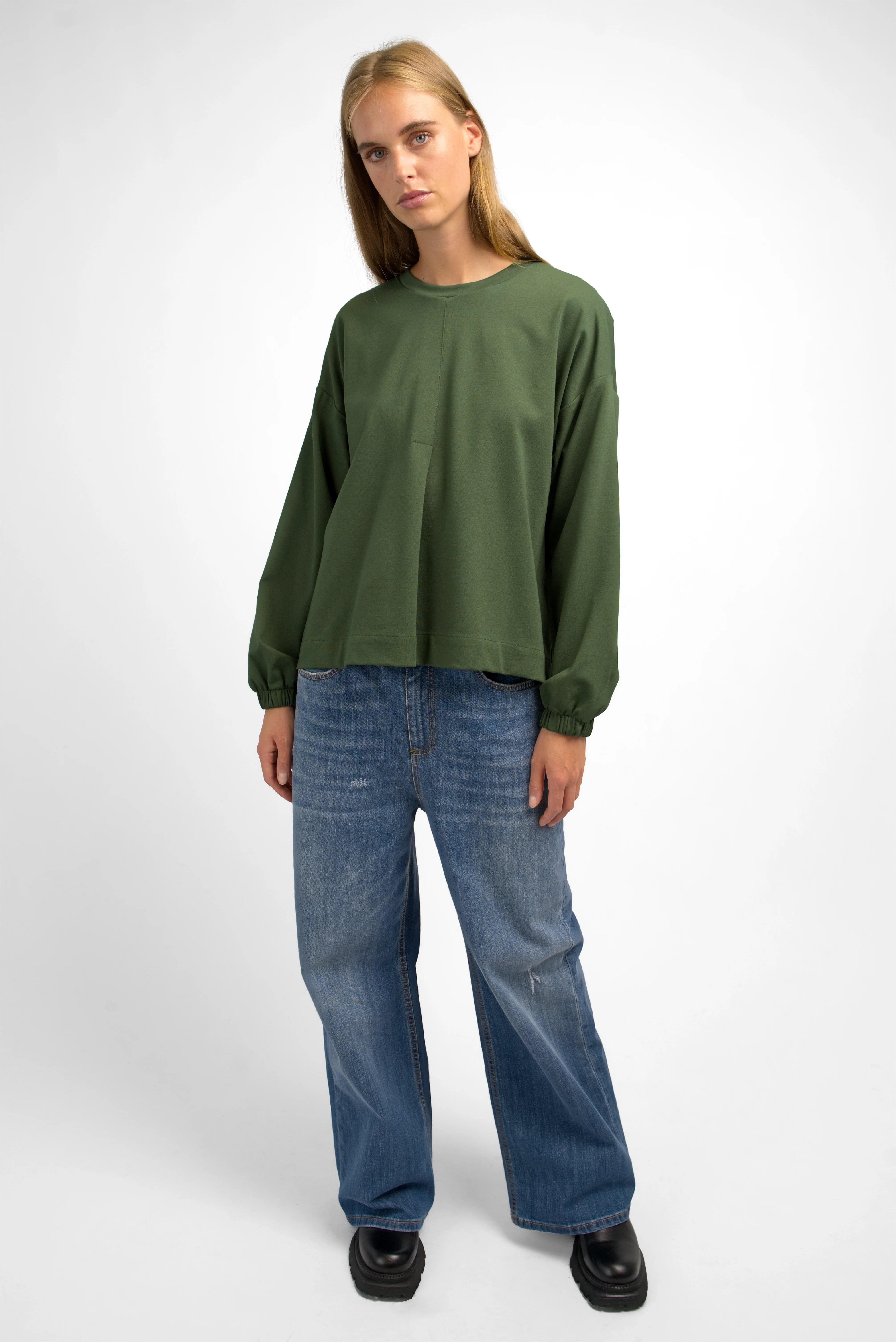 Woman wearing olive green HAGLA Shirt with relaxed fit, round neckline, elastic cuffs, and subtle front pleat.
