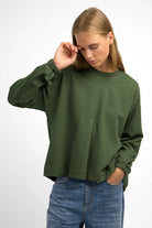 Woman wearing olive green HAGLA Shirt with relaxed fit, round neckline, elastic cuffs, and subtle front pleat