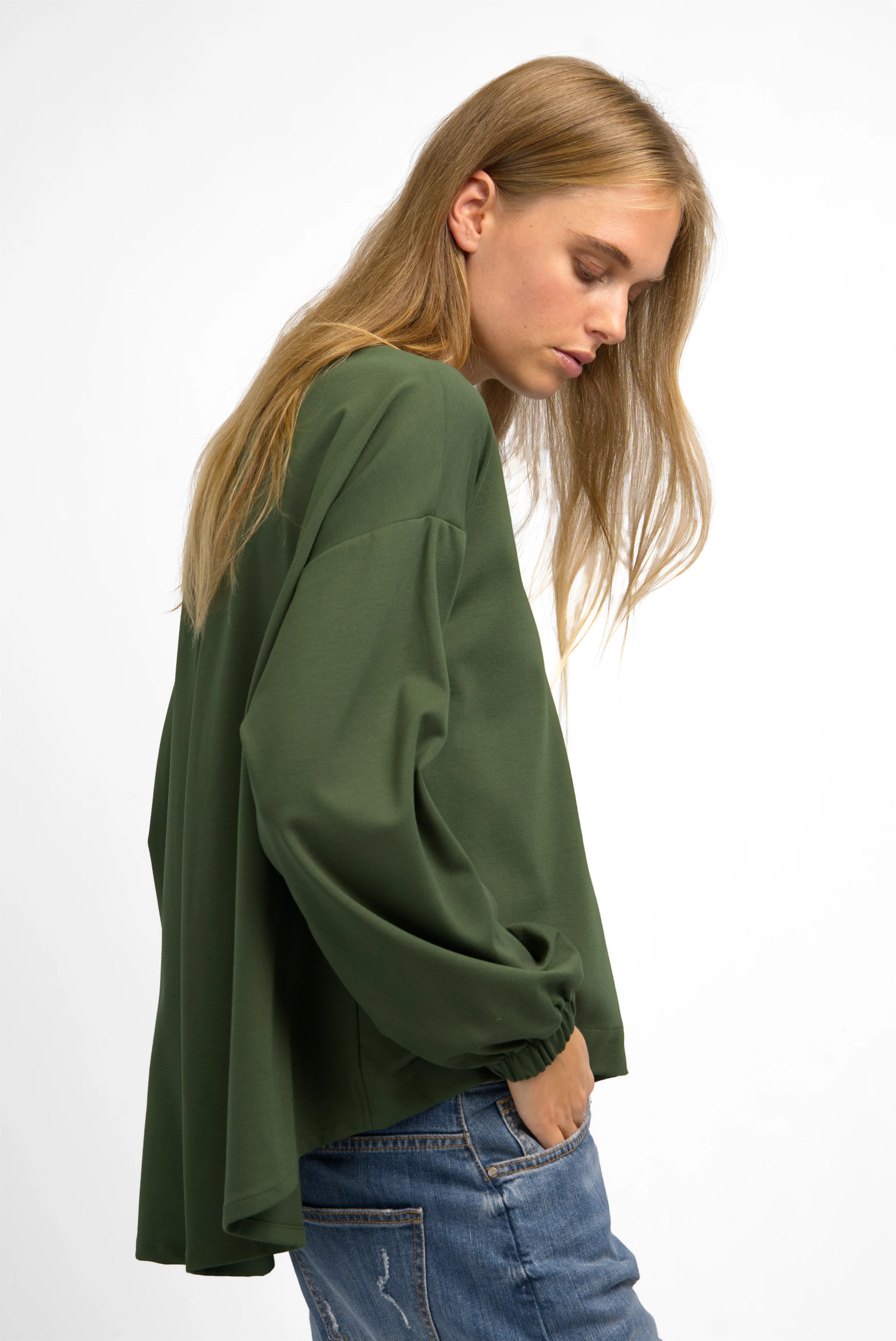 Woman wearing loose-fit olive green HAGLA Shirt with round neckline and elastic cuffs paired with jeans, side view