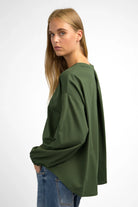 Woman wearing a relaxed fit olive green HAGLA Shirt with round neckline and elastic cuffs, featuring a back pleat and longer back hem