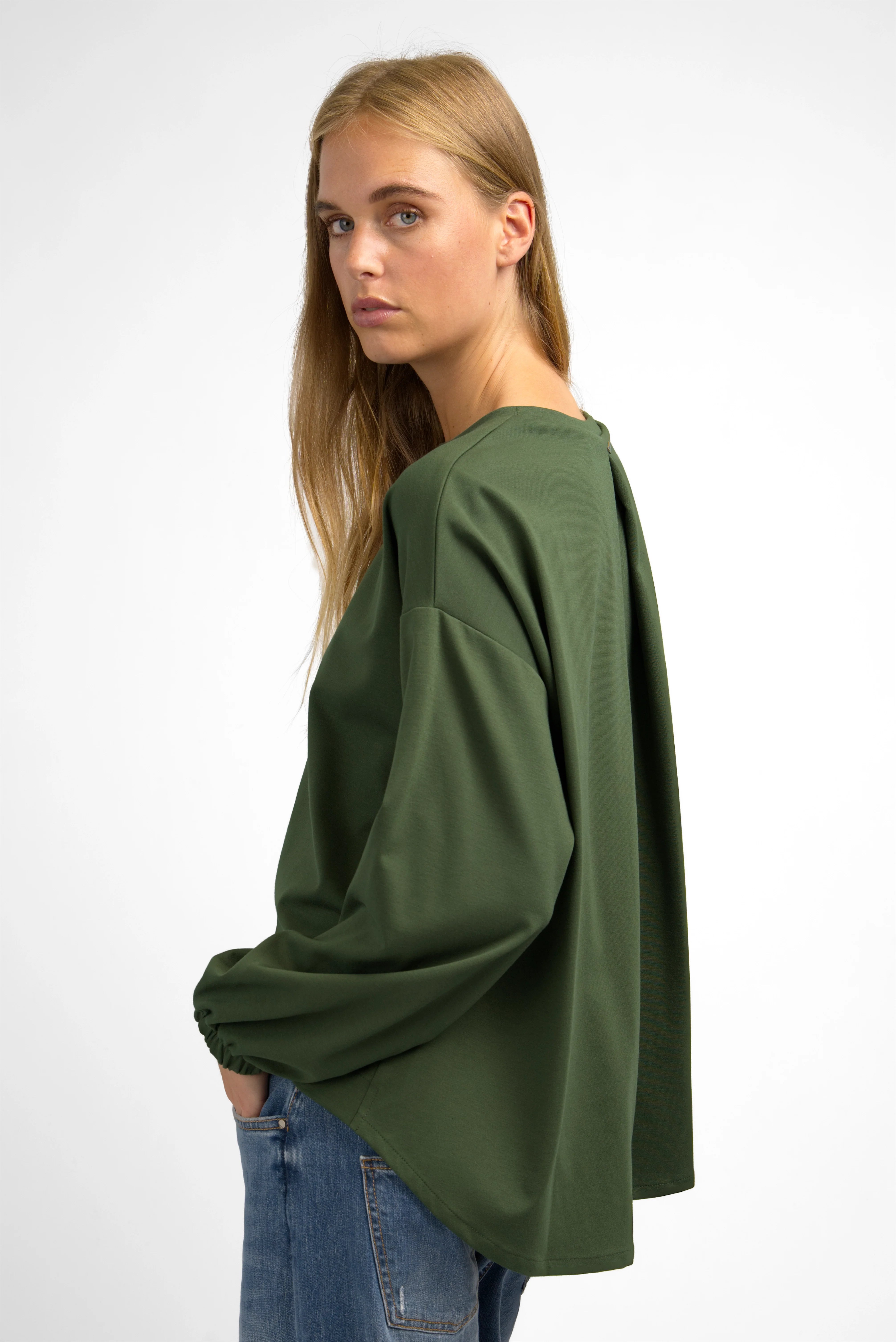 Woman wearing a relaxed fit olive green HAGLA Shirt with round neckline and elastic cuffs, featuring a back pleat and longer back hem