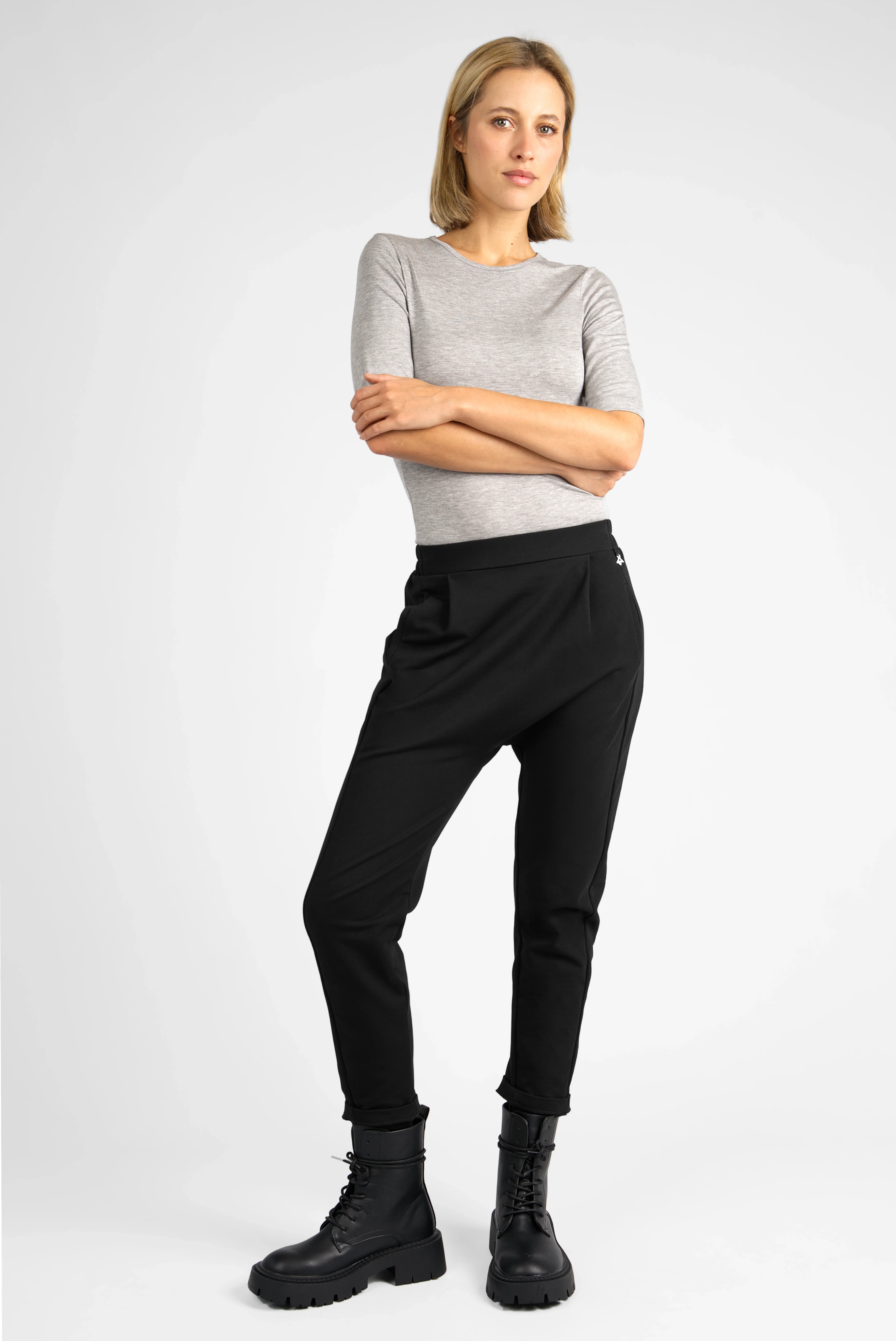 Frau trägt schwarze HANNA.K Tapered Sweathose mit elastischem Bund und Taschen, kombiniert mit grauem Oberteil und schwarzen Boots.