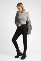 Frau trägt schwarze HANNA.K Tapered Sweathose mit tiefem Sitz und schmal zulaufendem Bein, kombiniert mit grauem Pullover und Cardigan.
