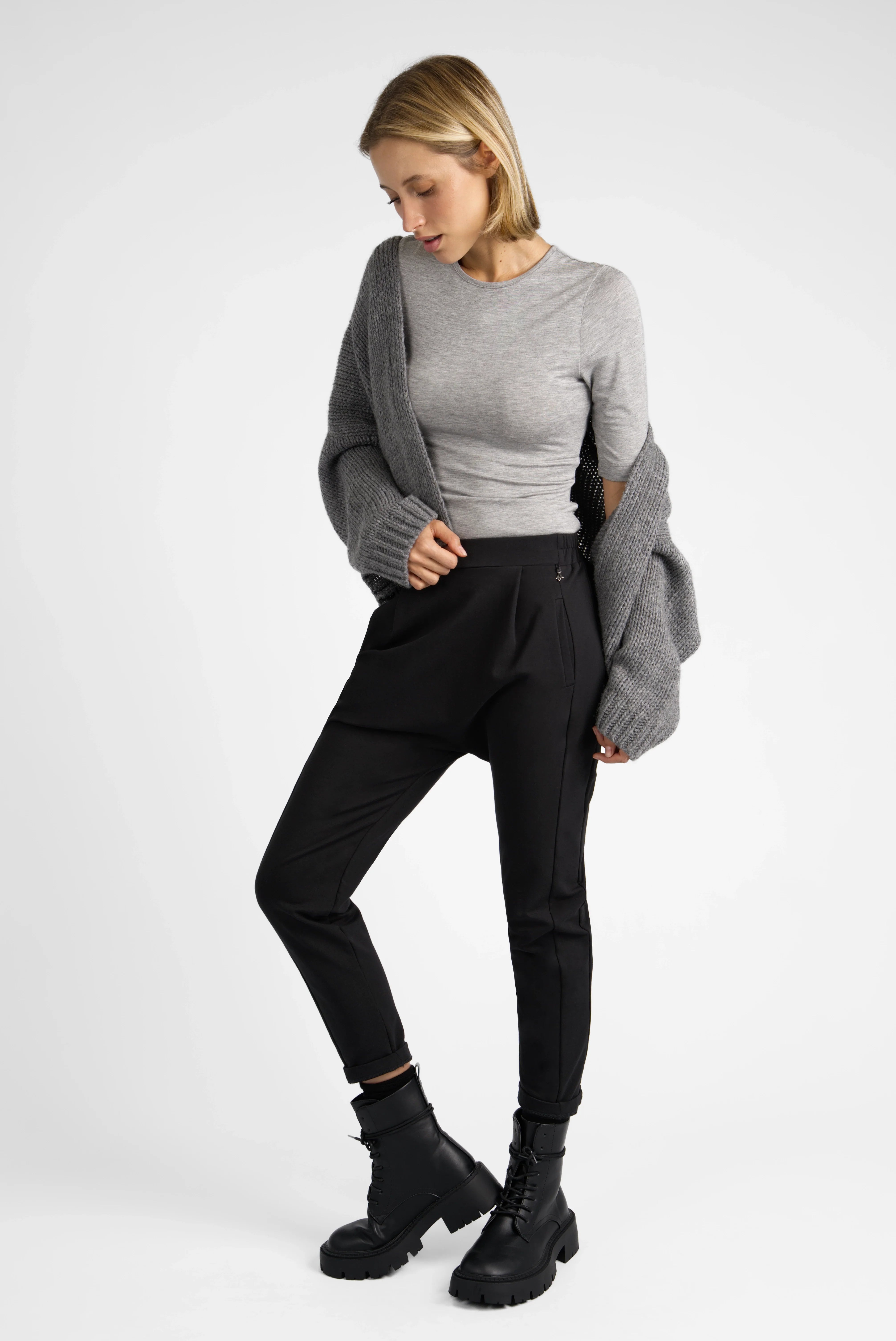 Frau trägt schwarze HANNA.K Tapered Sweathose mit tiefem Sitz und schmal zulaufendem Bein, kombiniert mit grauem Pullover und Cardigan.