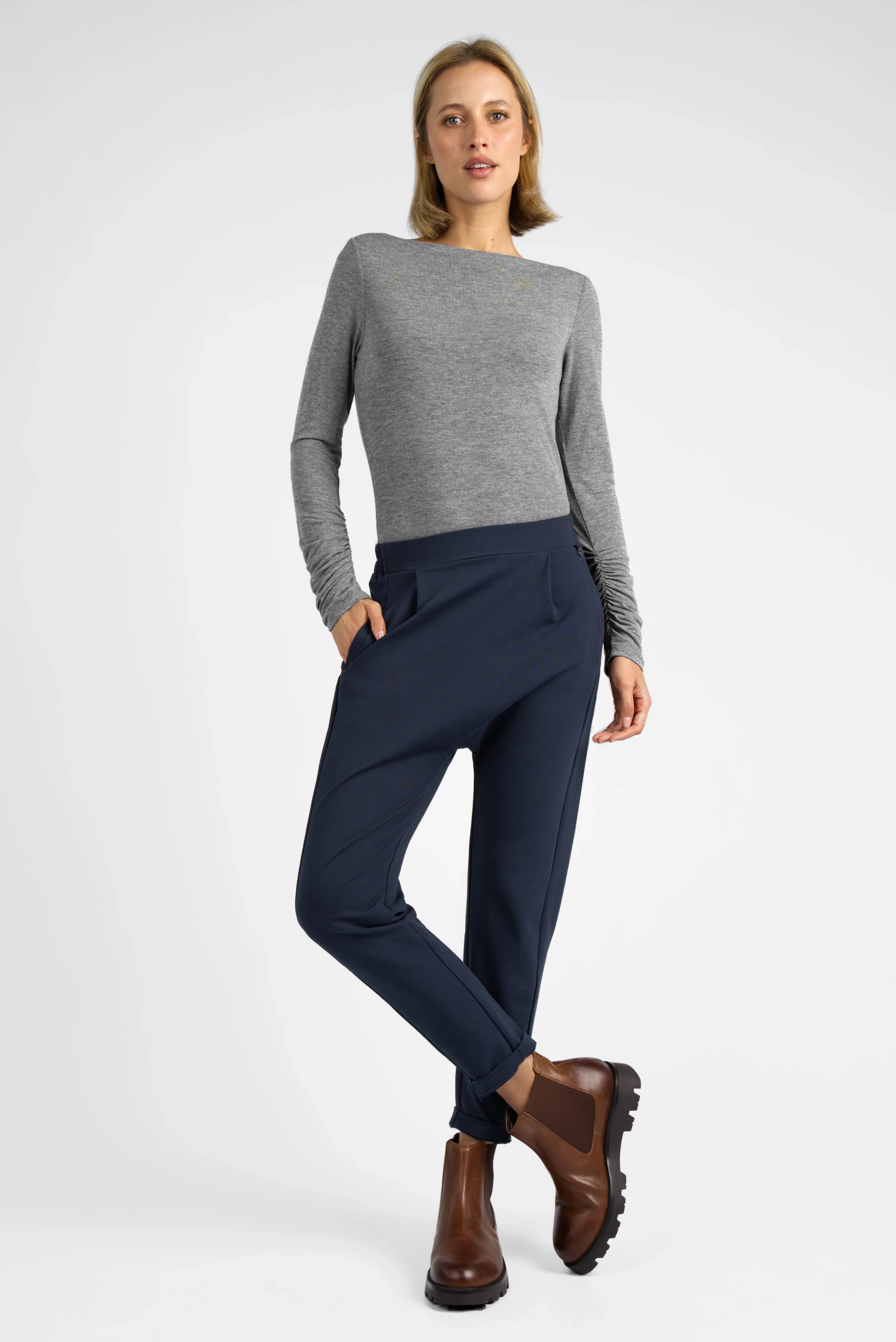 HANNA.K Tapered Sweathose in Navy mit tapered Bein, elastischem Bund und tiefem Schritt, kombiniert mit grauem Langarmshirt und braunen Stiefeln.