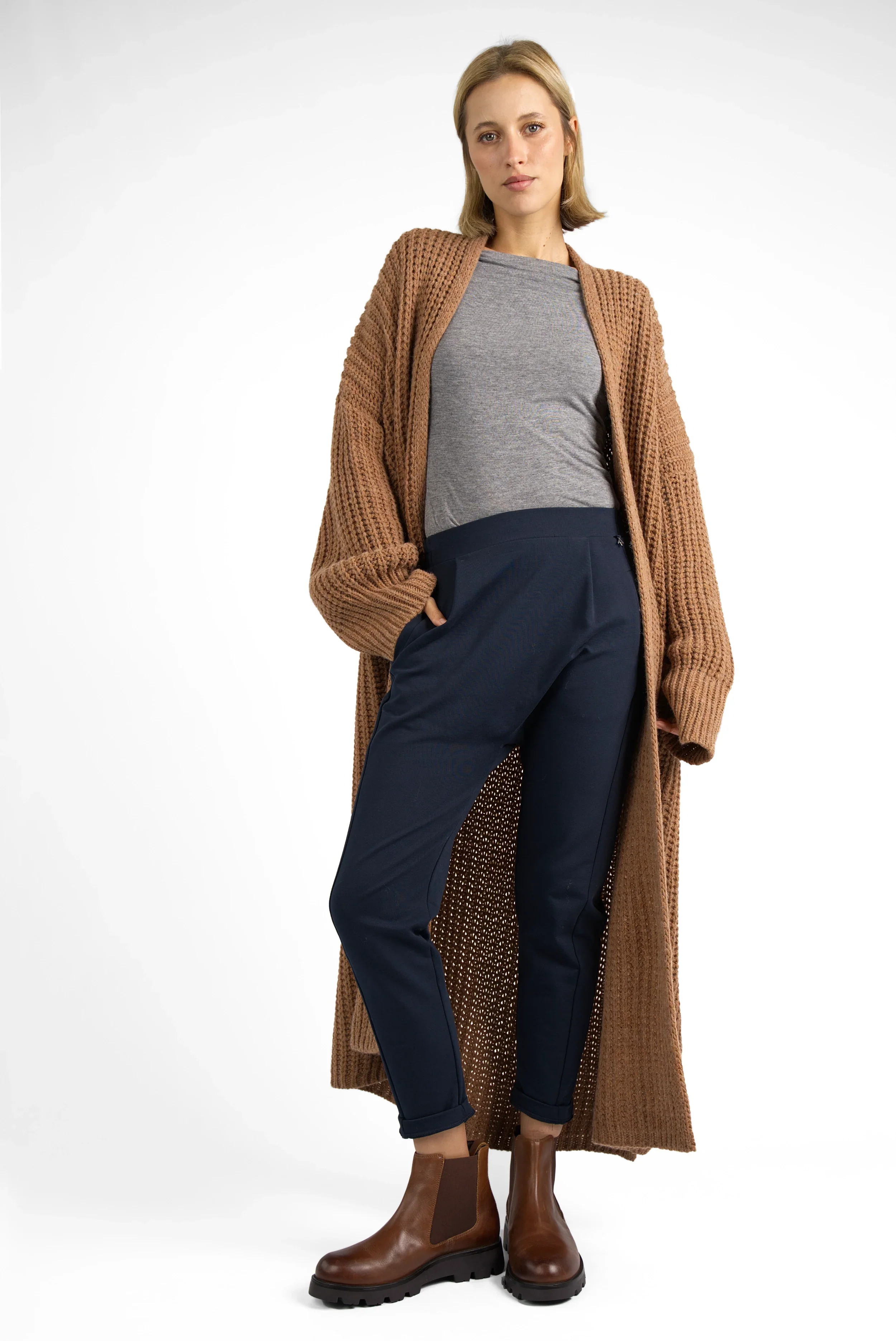 Frau trägt HANNA.K Tapered Sweathose in Dunkelblau mit elastischem Bund und Taschen, kombiniert mit grauem Shirt, langem braunem Strickmantel und braunen Stiefeln