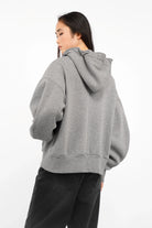 Gray relaxed fit zip-hoodie with oversized sleeves and hood worn by a woman from the back