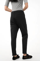 Black tapered pants with relaxed hip fit and narrow legs, worn with casual shoes and grey top, showcasing the back view.