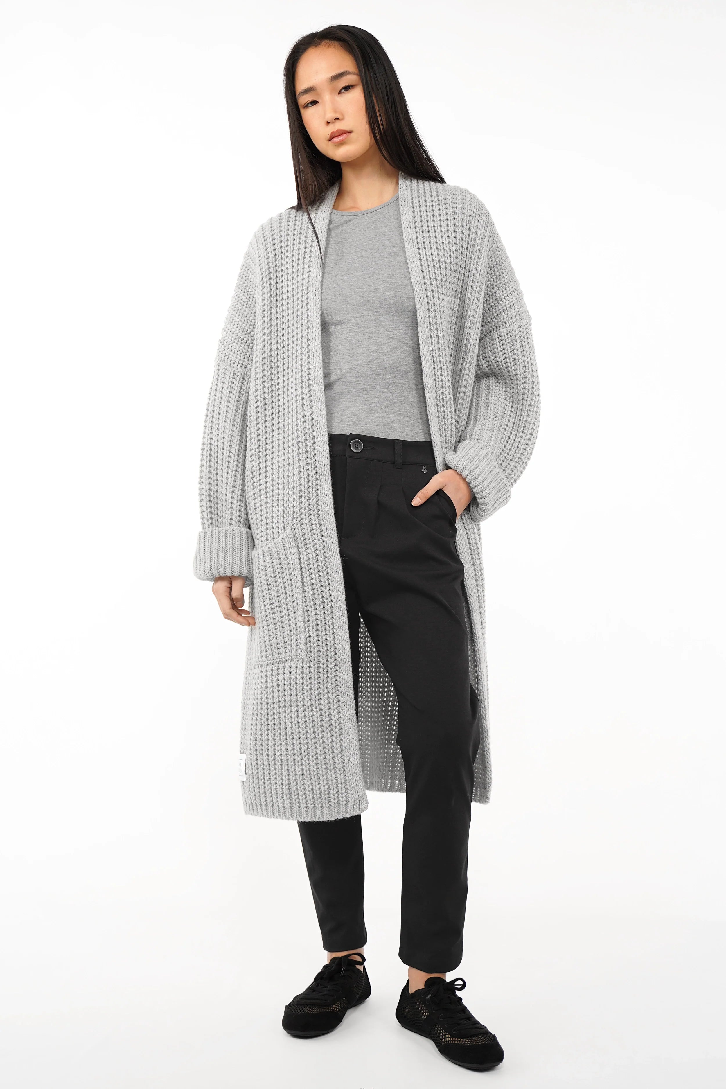 Frau trägt schwarze Heelena Tapered Pants mit grauem Pullover und langer Strickjacke