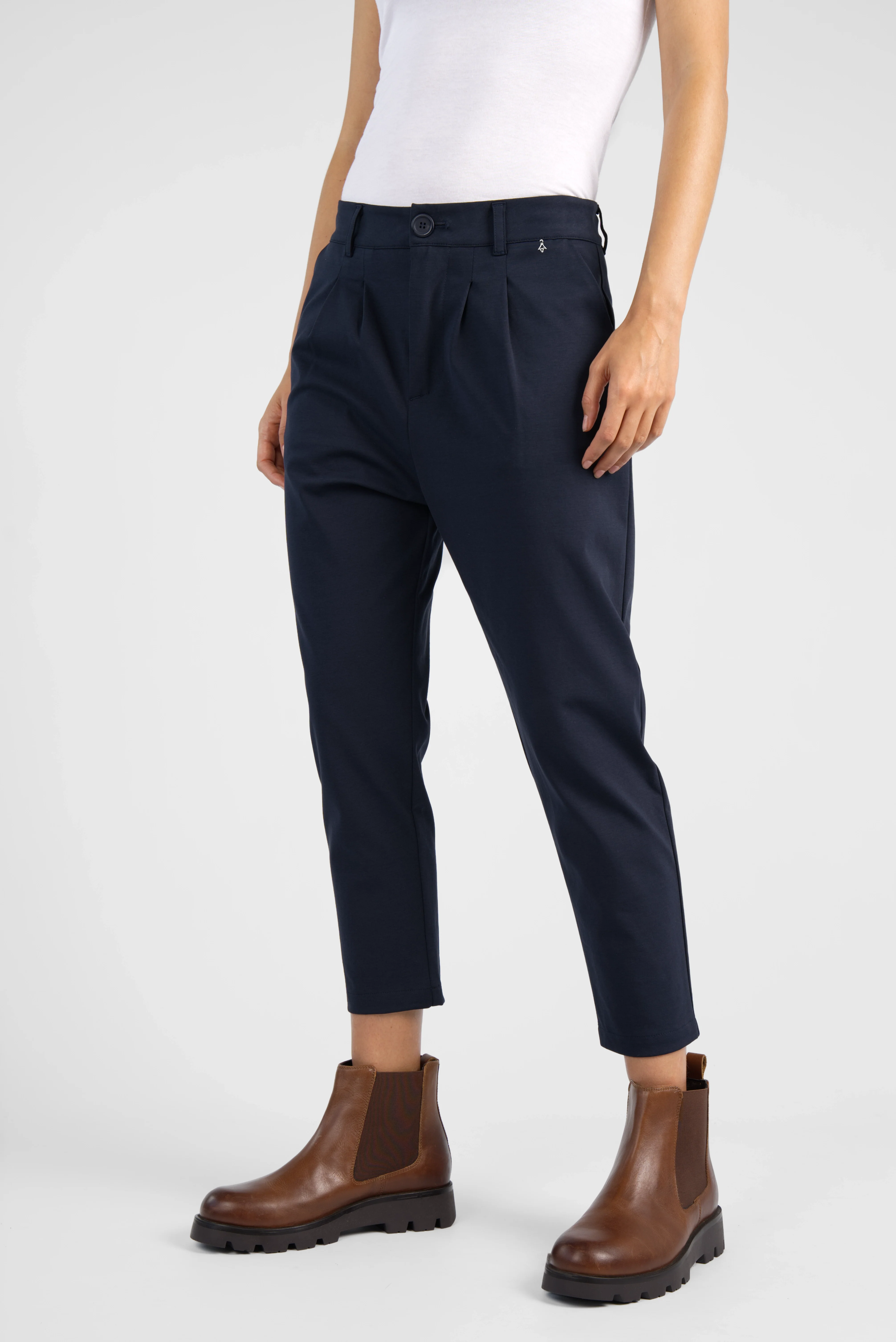 Damen HEELENA OG Tapered Pants cropped in Dunkelblau mit schmal zulaufendem Bein und leichter Bundfalte, kombiniert mit braunen Stiefeletten.