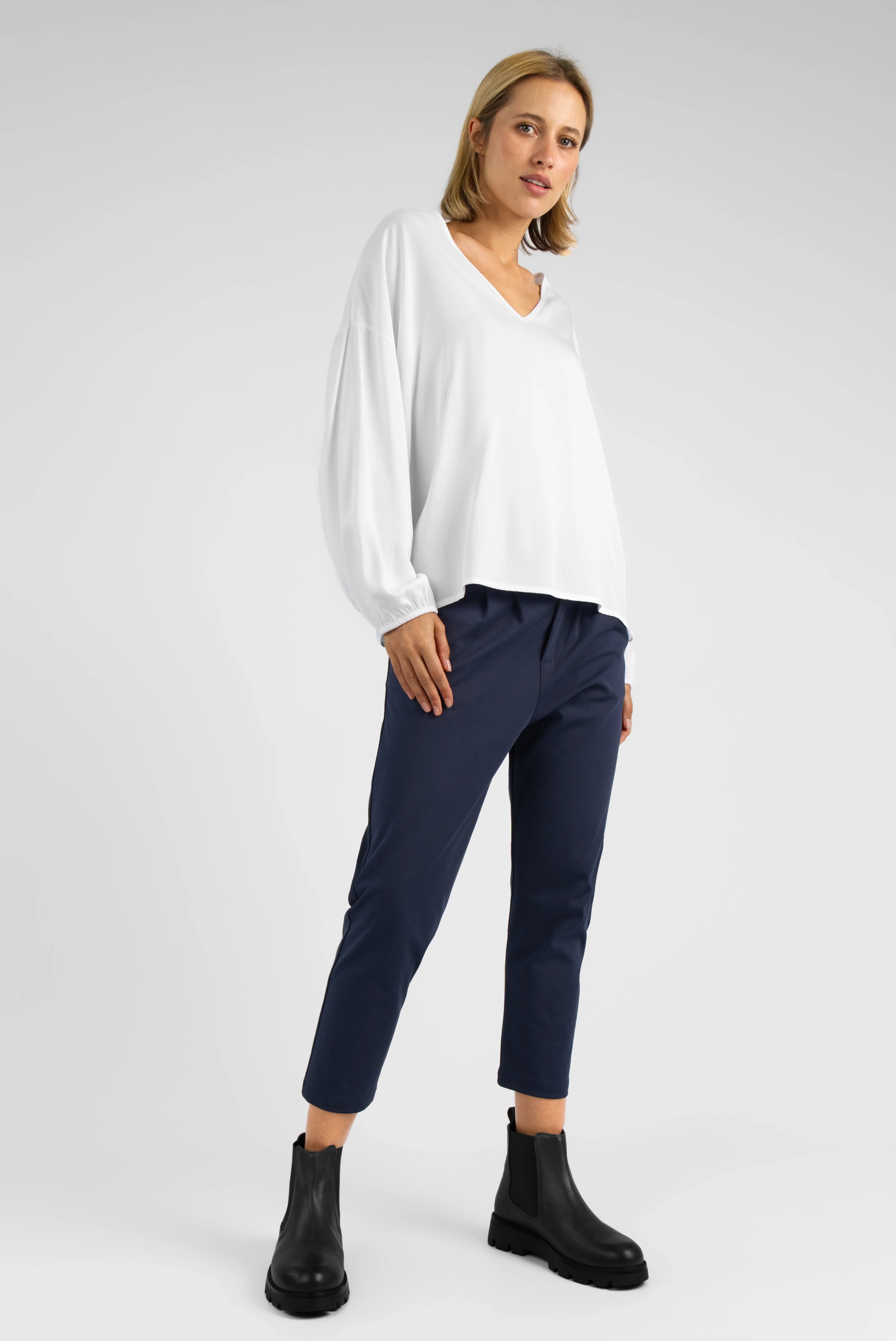 Frau trägt HEELENA OG Tapered Pants cropped in Dunkelblau mit schwarzer Stiefelette und weißem Pullover