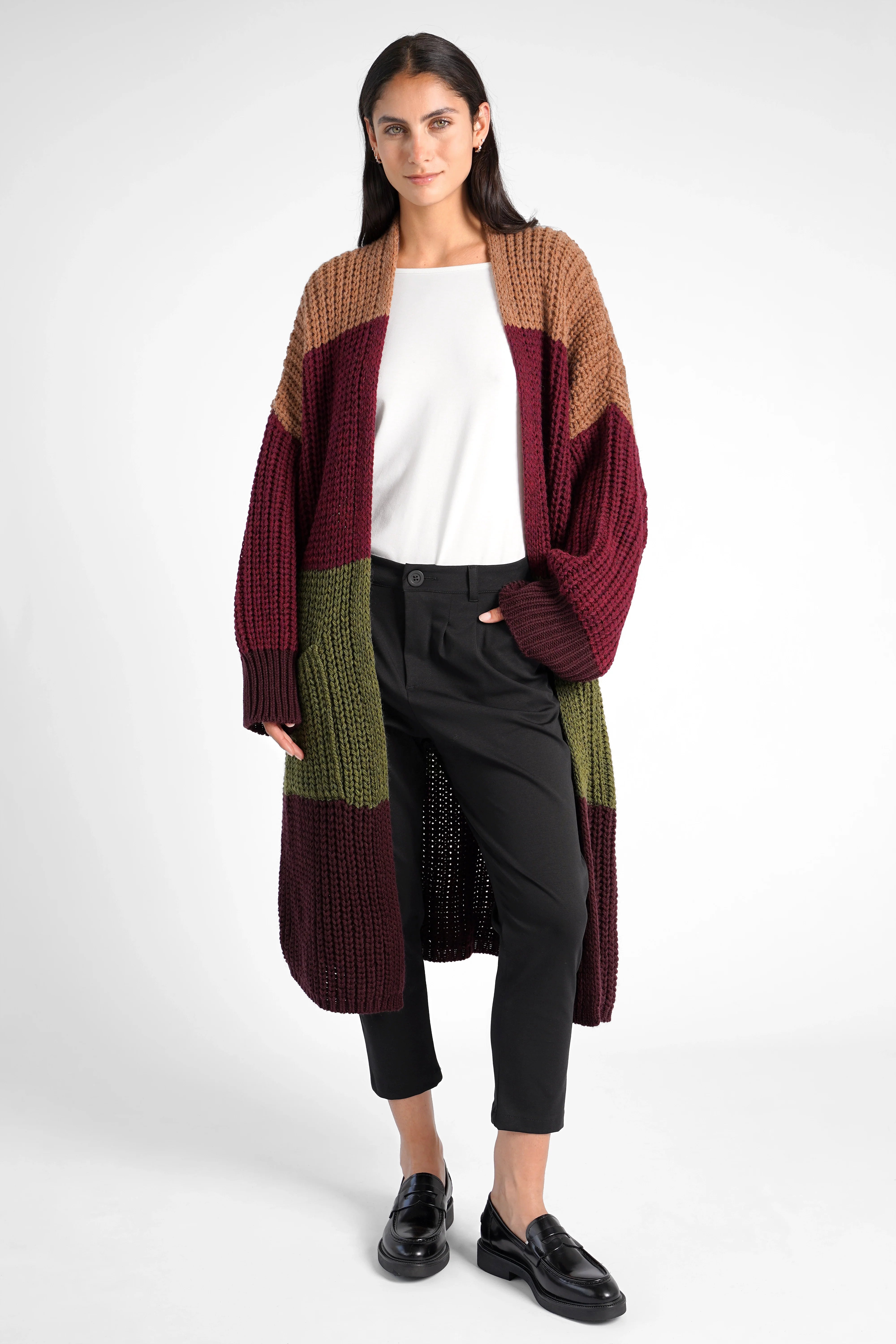 Frau trägt schwarze HEELENA OG Tapered Pants cropped mit weißem Oberteil und langem mehrfarbigem Strickcardigan