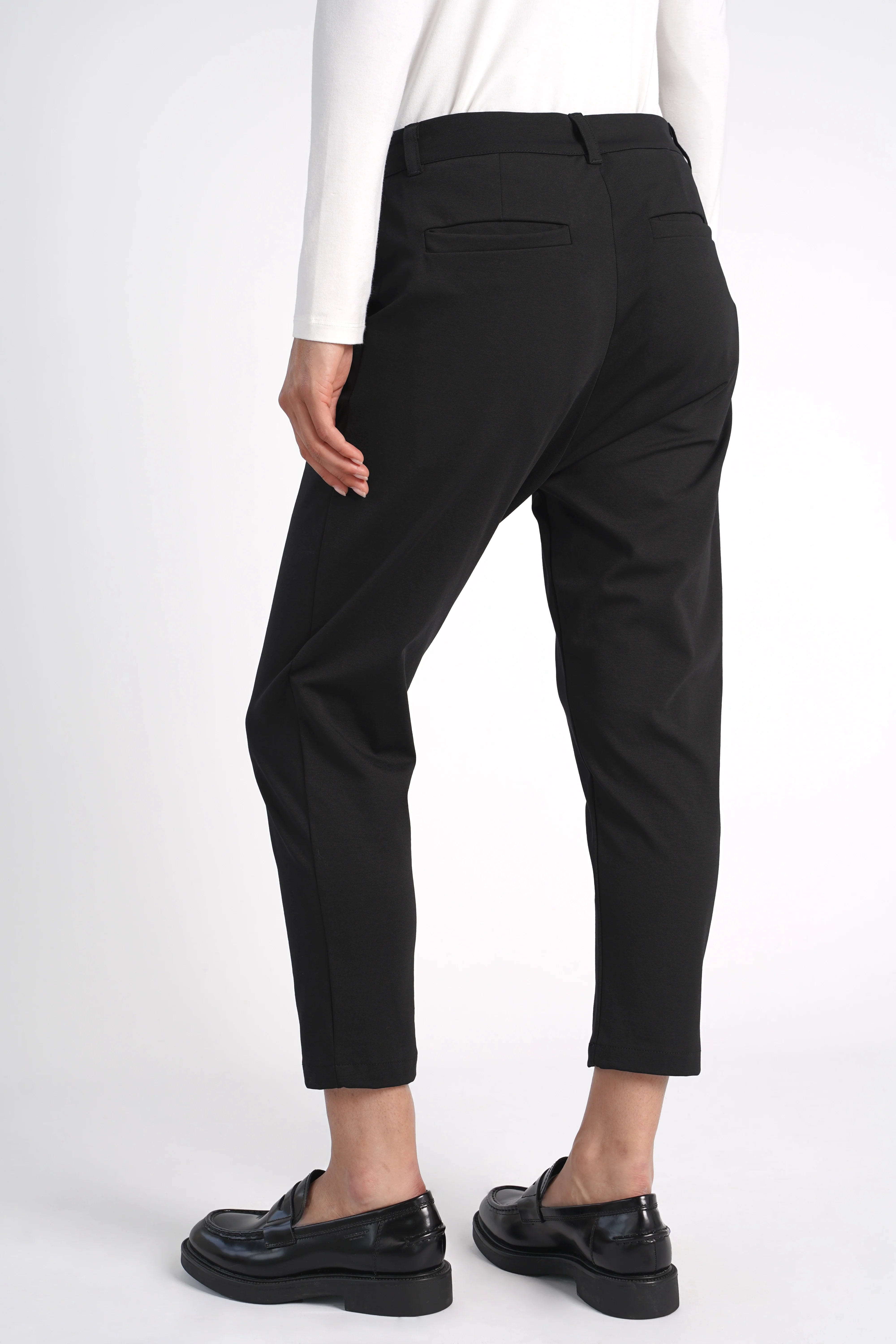 Schwarze HEELENA OG Tapered Pants cropped mit schmal zulaufendem Bein und normaler Bundhöhe, getragen mit schwarzen Slippern.