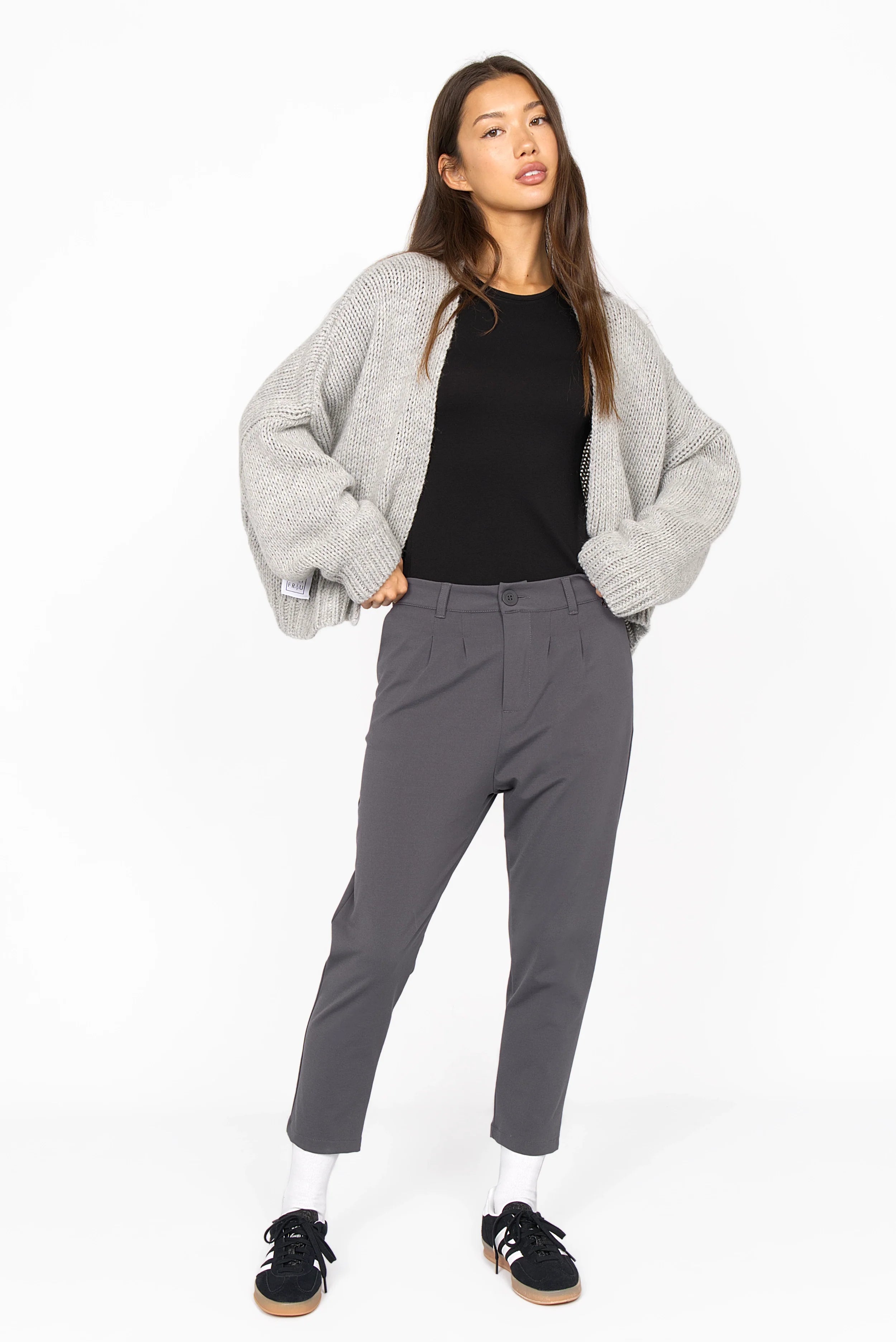 Frau trägt graue HEELENA OG Tapered Pants cropped mit schwarzem Shirt und grauer Strickjacke, sportlicher Look