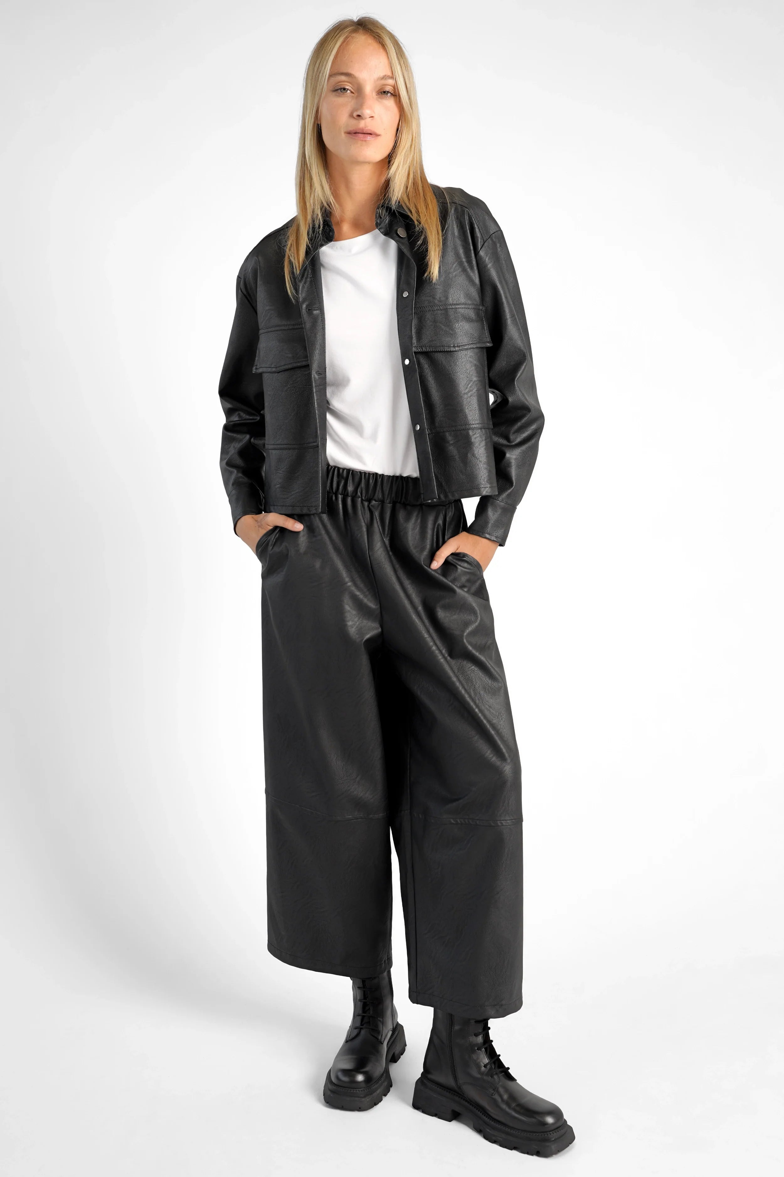 Woman wearing black HERA Wide Leg Hose with elastic waistband, side pockets, and relaxed fit styled with a black jacket and boots.