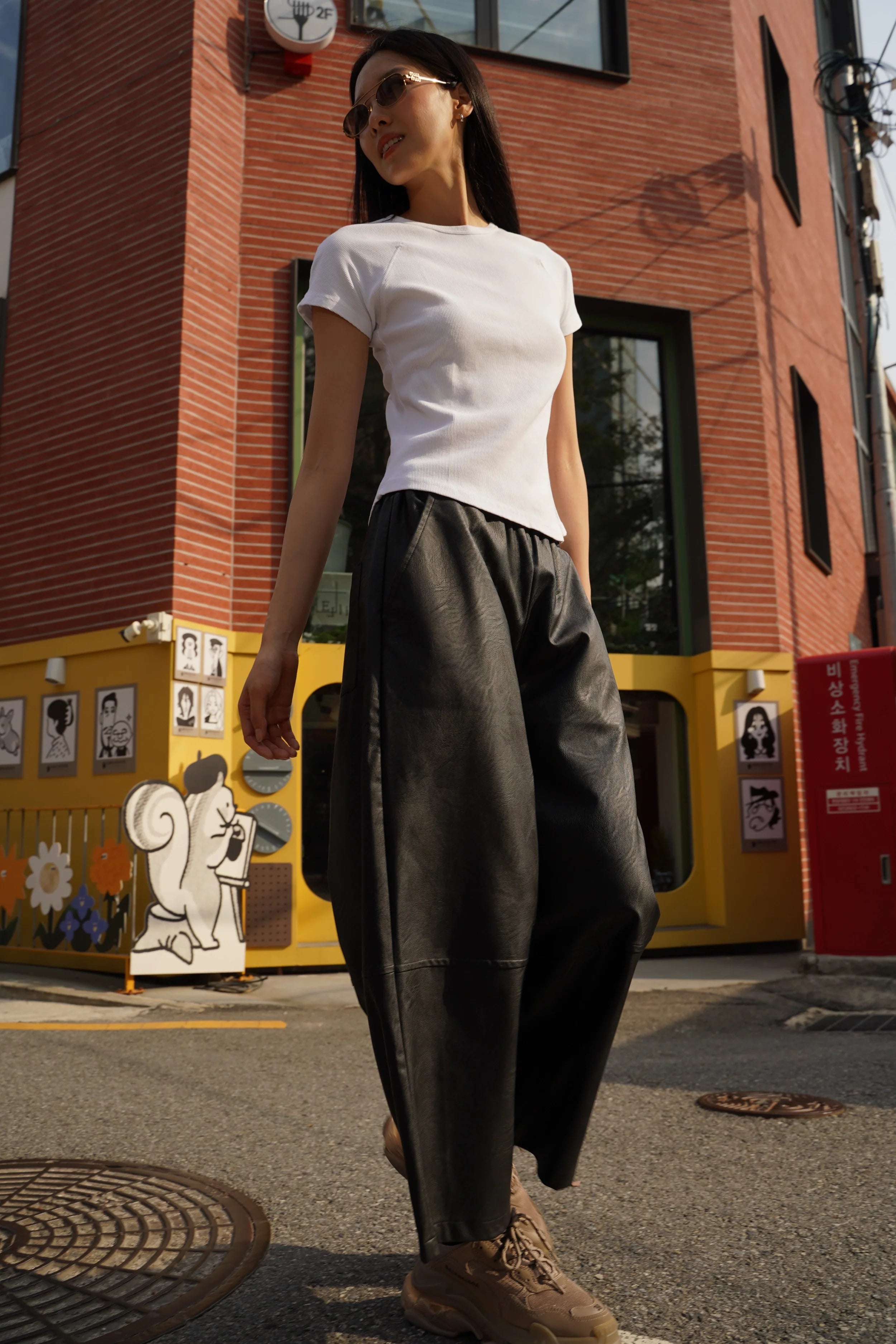Damen trägt HERA Wide Leg Hose in Lederoptik mit weißem T-Shirt und Sneakern urban kombiniert