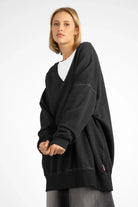 Woman wearing oversized black IMIKO Studio Long-Sweater with deep V-neck and dropped shoulders