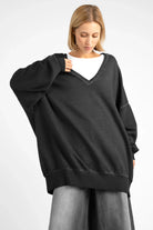 Woman wearing oversized black IMIKO Studio Long-Sweater with deep V-neck and dropped shoulders