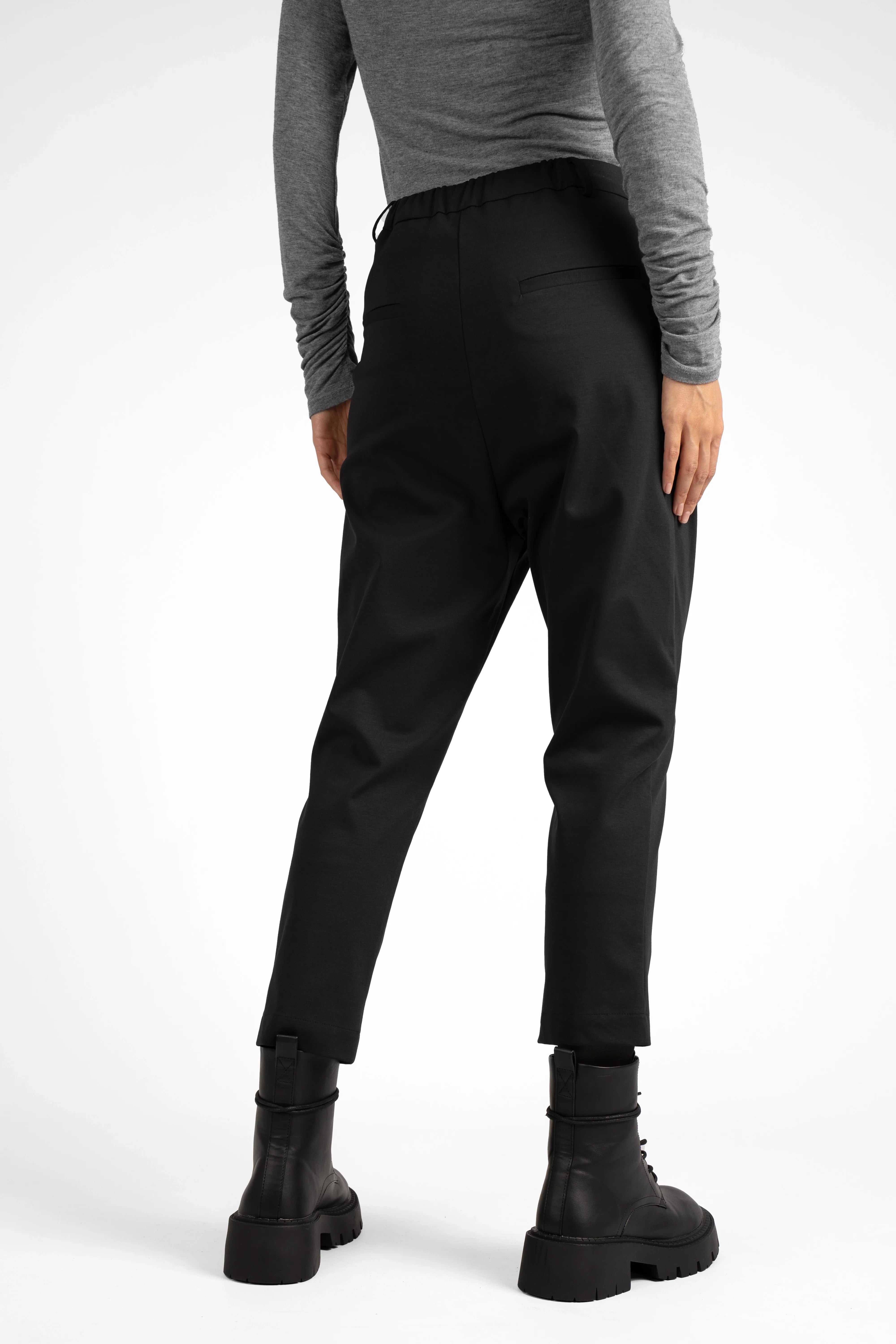Back view of a person wearing black JALDI cropped tapered pants with elastic waistband and slim tapered legs paired with black boots and a gray long-sleeve top