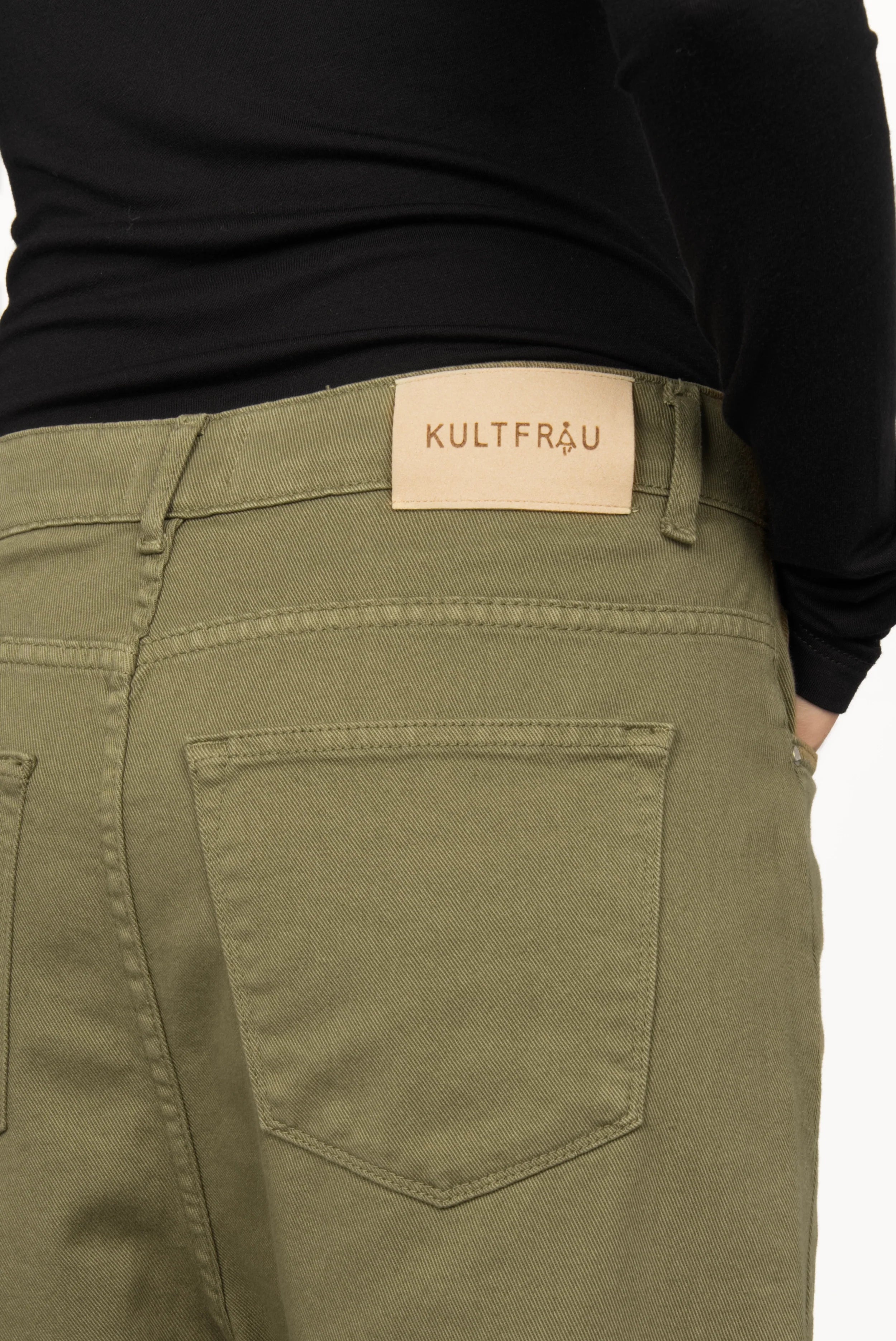 Close-up view of olive green baggy jeans with back pockets and branded leather patch on waistband, worn with a black top.