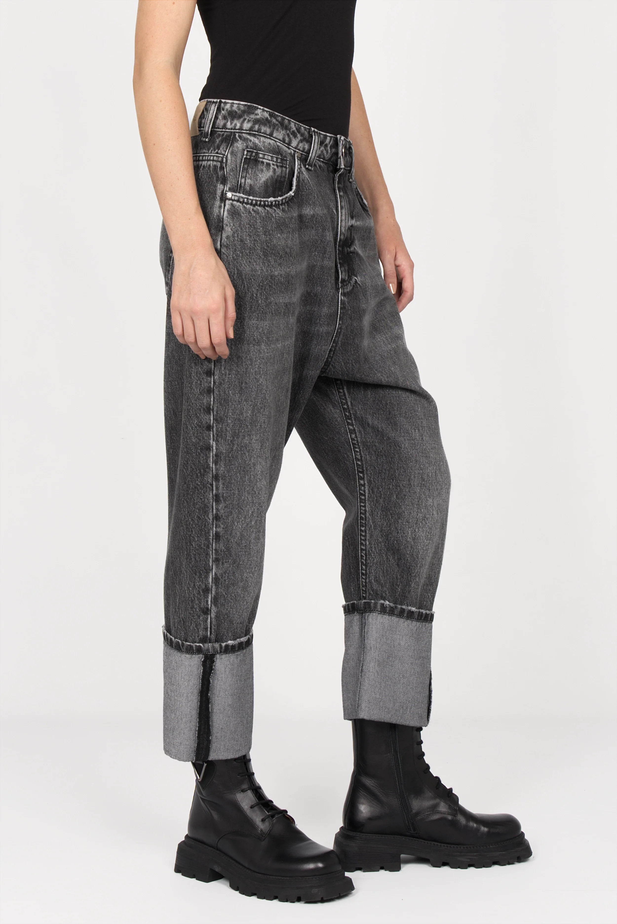 Black washed baggy jeans with wide fixed cuffs and relaxed fit on model wearing black boots and top.