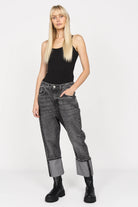 Woman wearing black tank top and gray baggy jeans with wide roll-up cuffs and black boots against white background