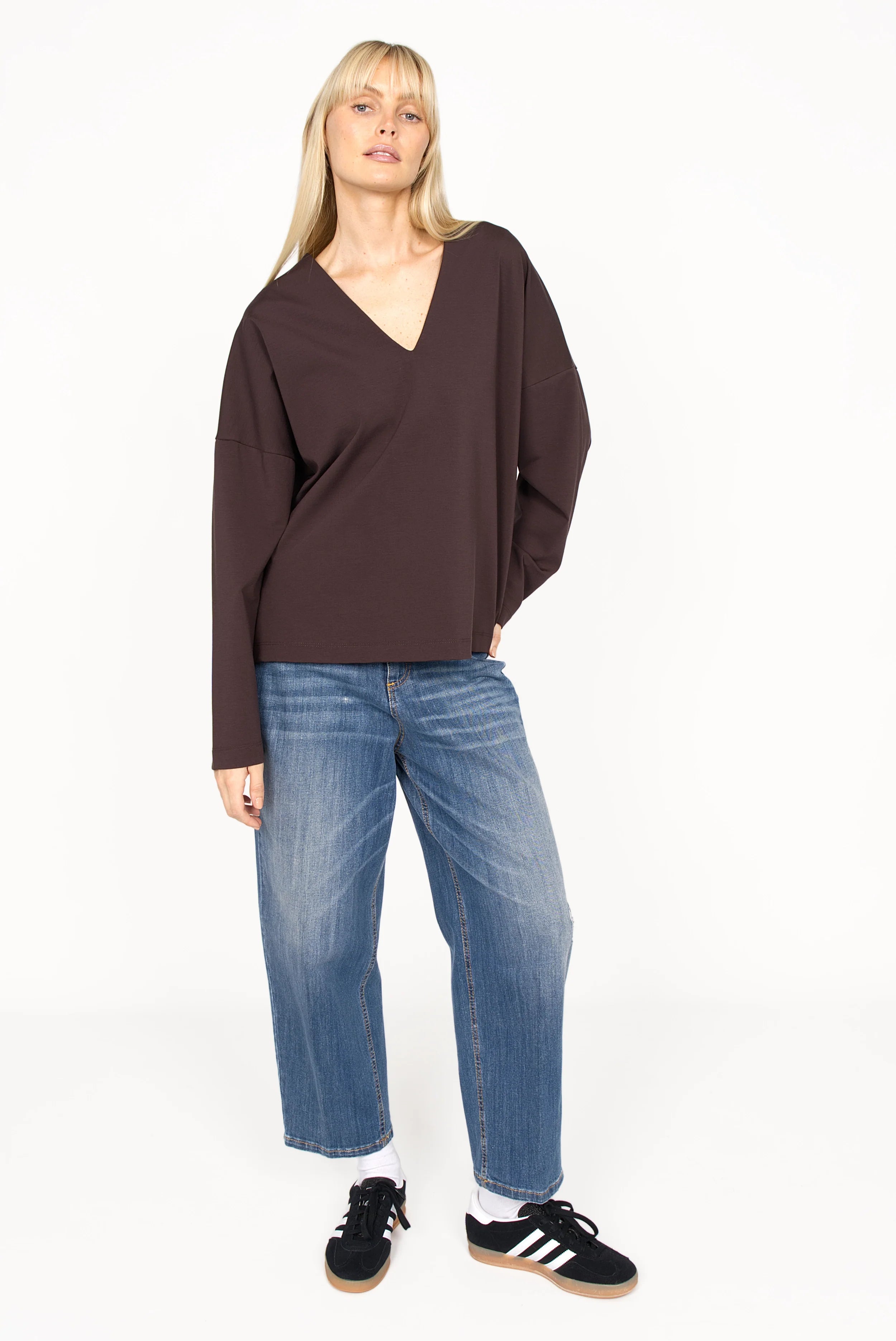 Woman wearing JEEBY Loose-Fit Jeans with high waist and tapered wide legs styled with a dark brown V-neck top and black sneakers.