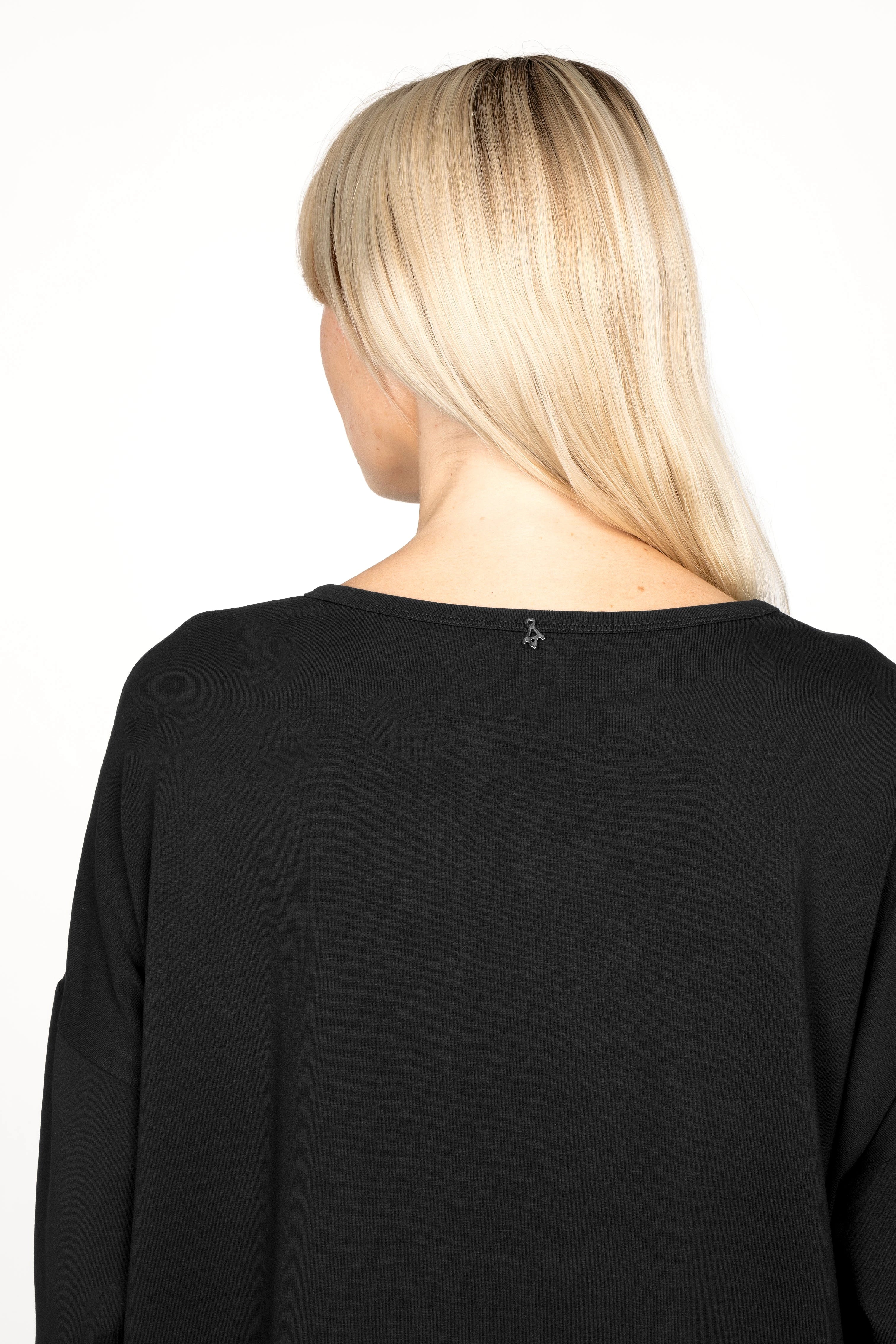 Frau trägt JENEN Oversized Longsleeve aus weichem Jersey-Viskose mit weitem Rundhalsausschnitt und überschnittenen Schultern in Schwarz, Rückansicht