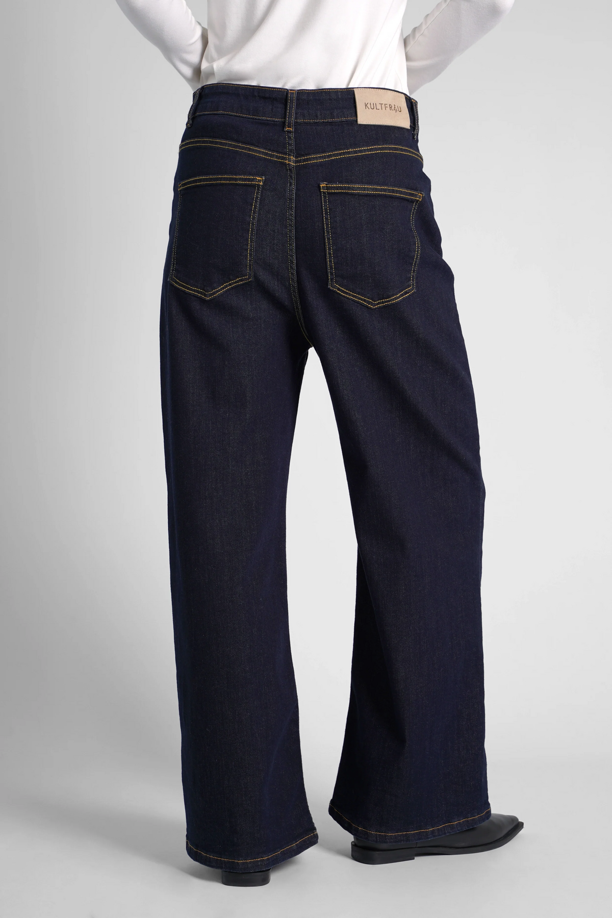 Rear view of dark blue wide-leg jeans on a model wearing a white top, showcasing back pockets and contrast stitching for Bildbearbeitung Test.