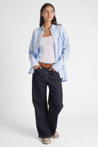 Damen trägt handgefertigte JOOSY Wide Leg Jeans mit Relaxed Fit und normaler Leibhöhe kombiniert mit hellblauer Bluse und braunem Gürtel
