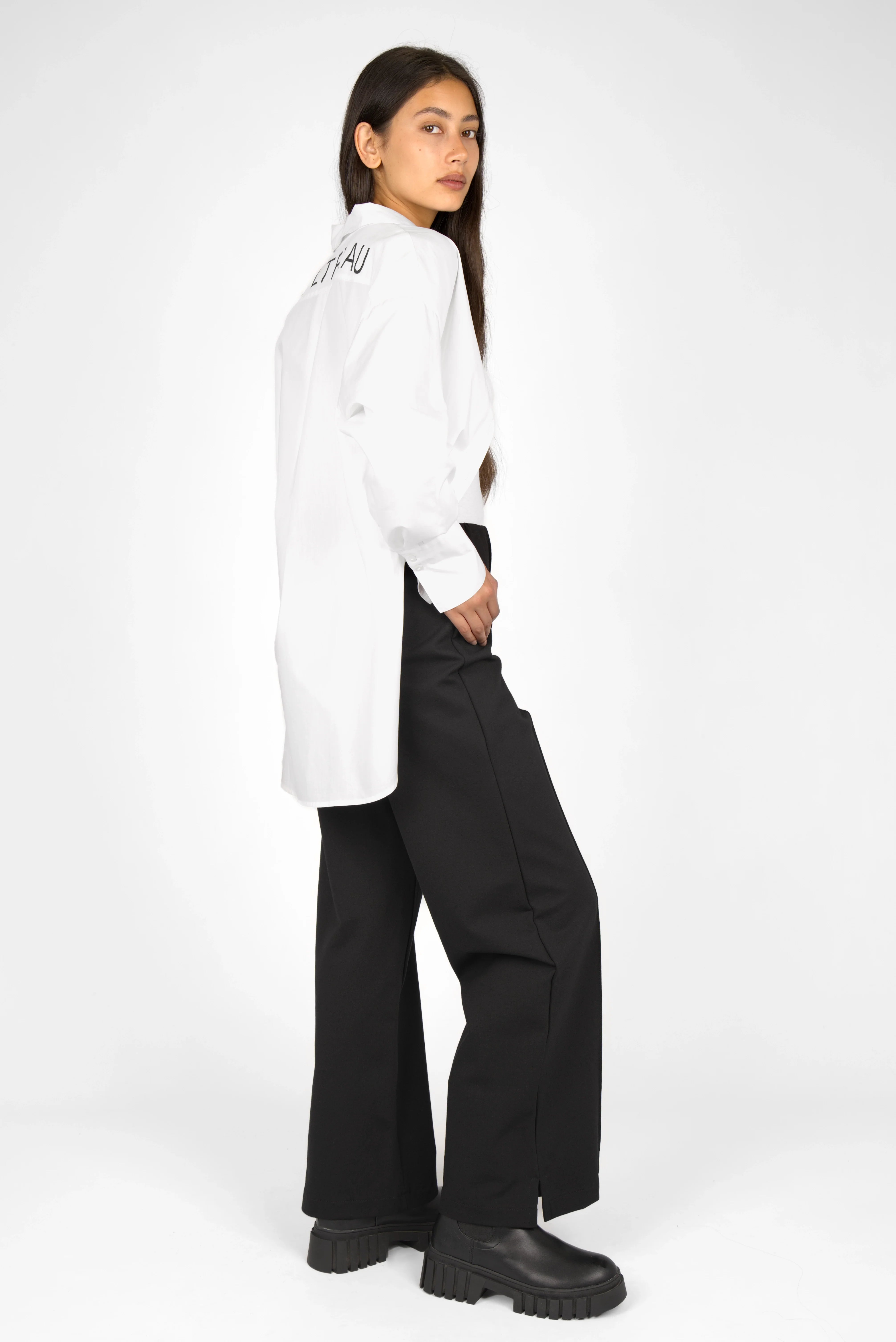 Woman wearing KANDANEA Gerade Hose in black with straight leg and small side slits, paired with a long white shirt and black boots.