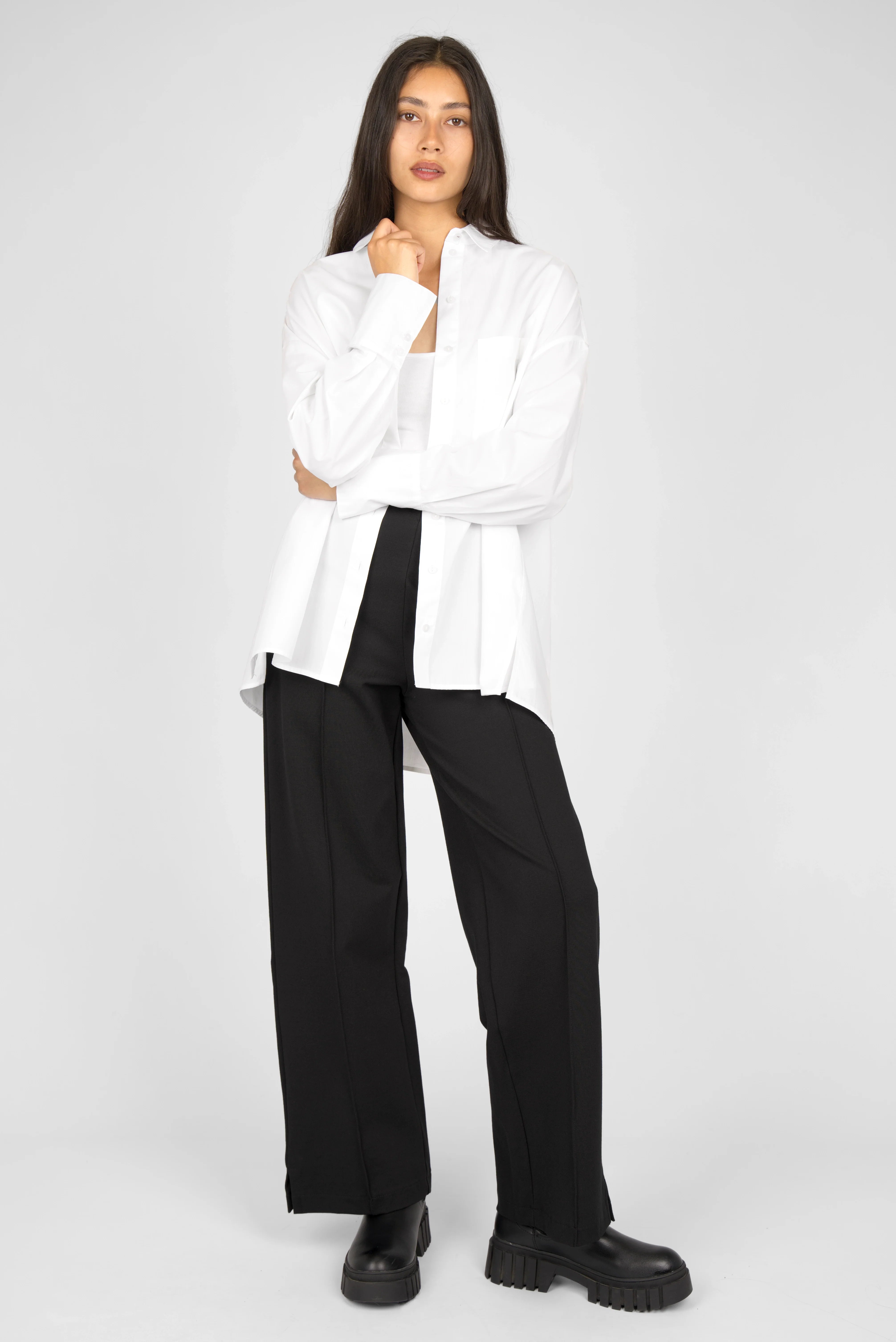 Woman wearing black KANDANEA Gerade Hose straight-leg pants with subtle front pleats and small hem slits paired with a white shirt and black boots