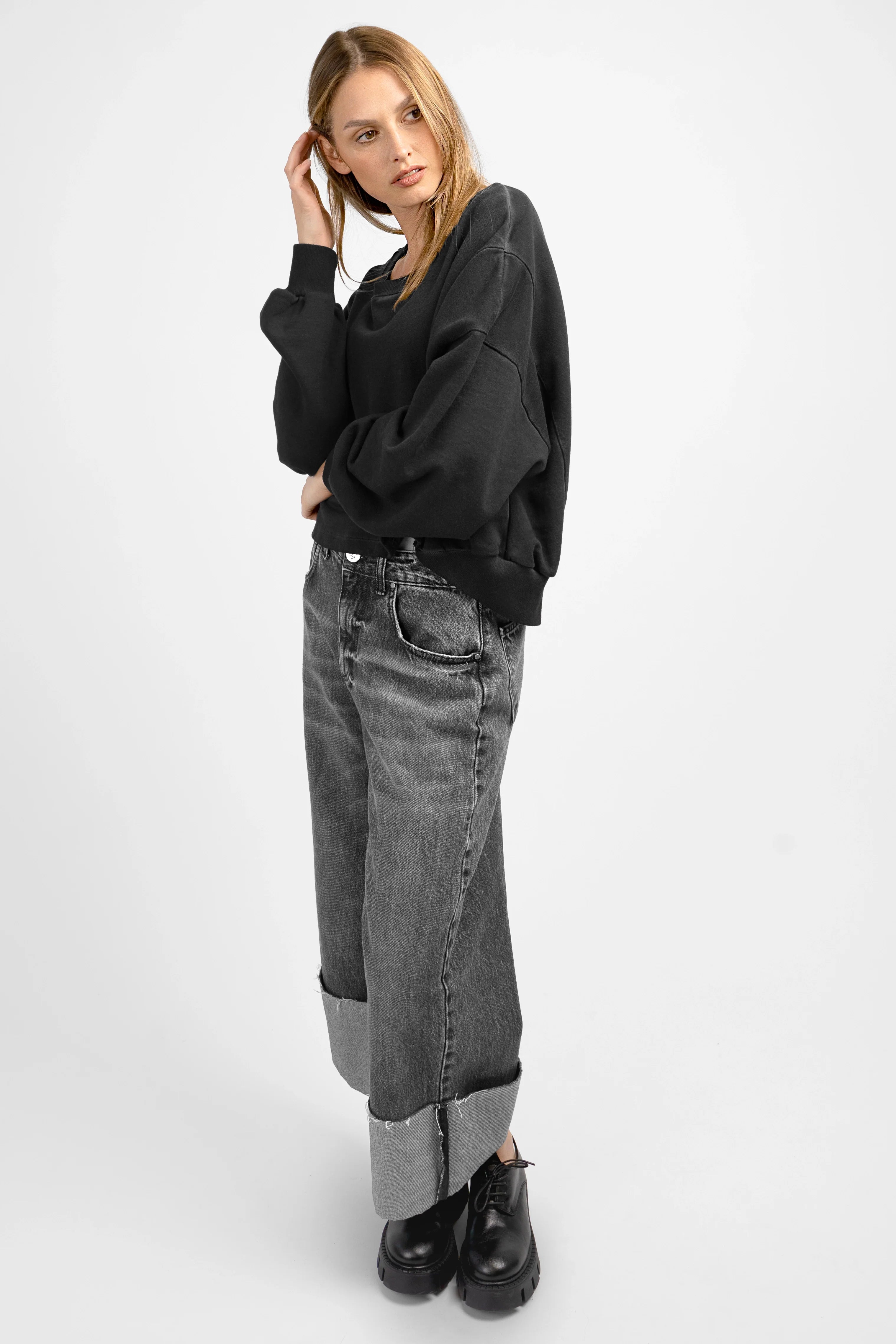 Woman wearing black KERY Cropped Sweater with oversized fit and U-boat neckline paired with cuffed wide-leg jeans and black shoes