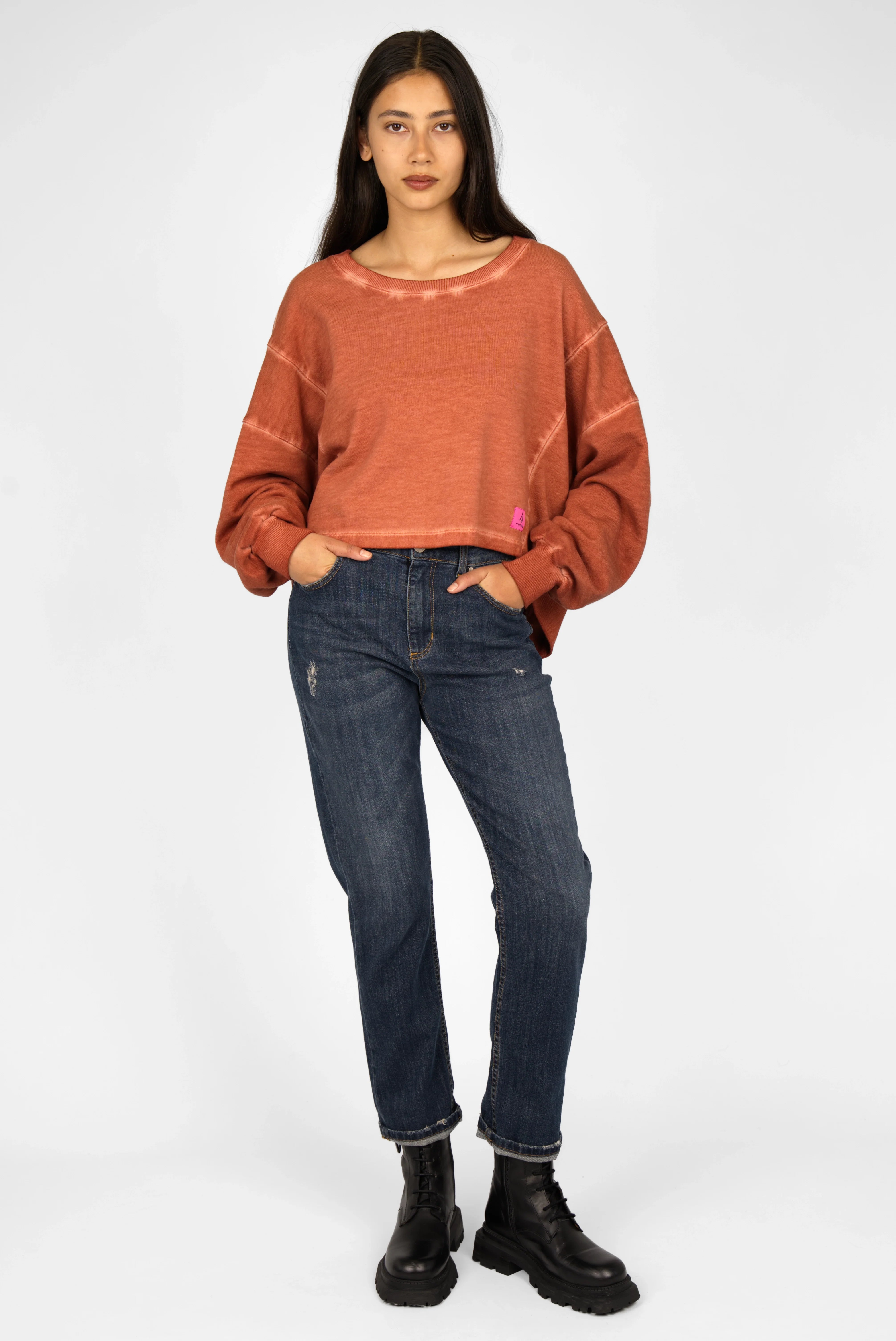 Woman wearing KERY Cropped Sweater in cold-washed cotton with oversized fit, cropped length, U-boat neckline, and pink STUDIO logo patch.
