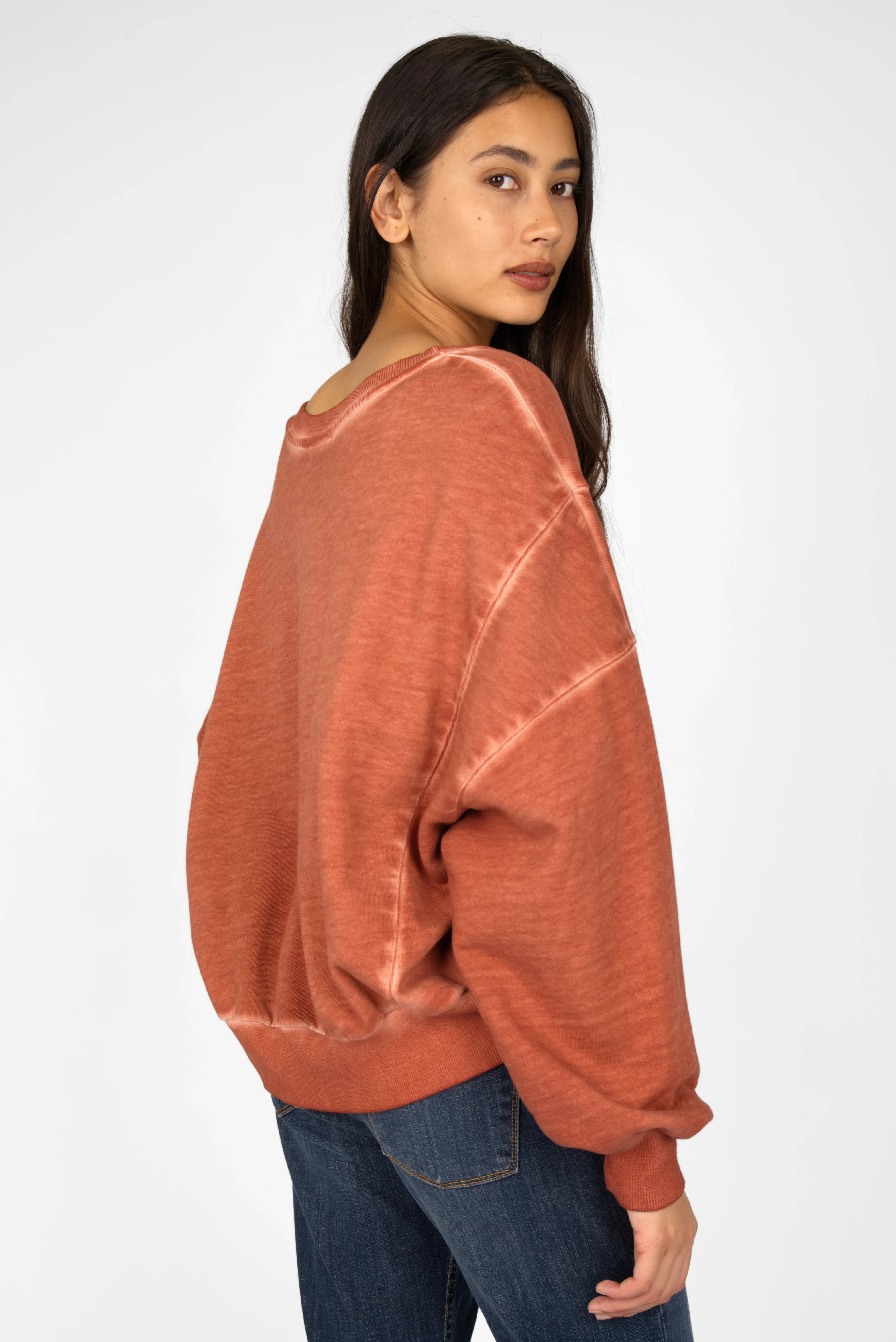 Woman wearing a rust-colored KERY Cropped Sweater with oversized fit and cold-washed cotton fabric, featuring a boat neckline and extended back hem.