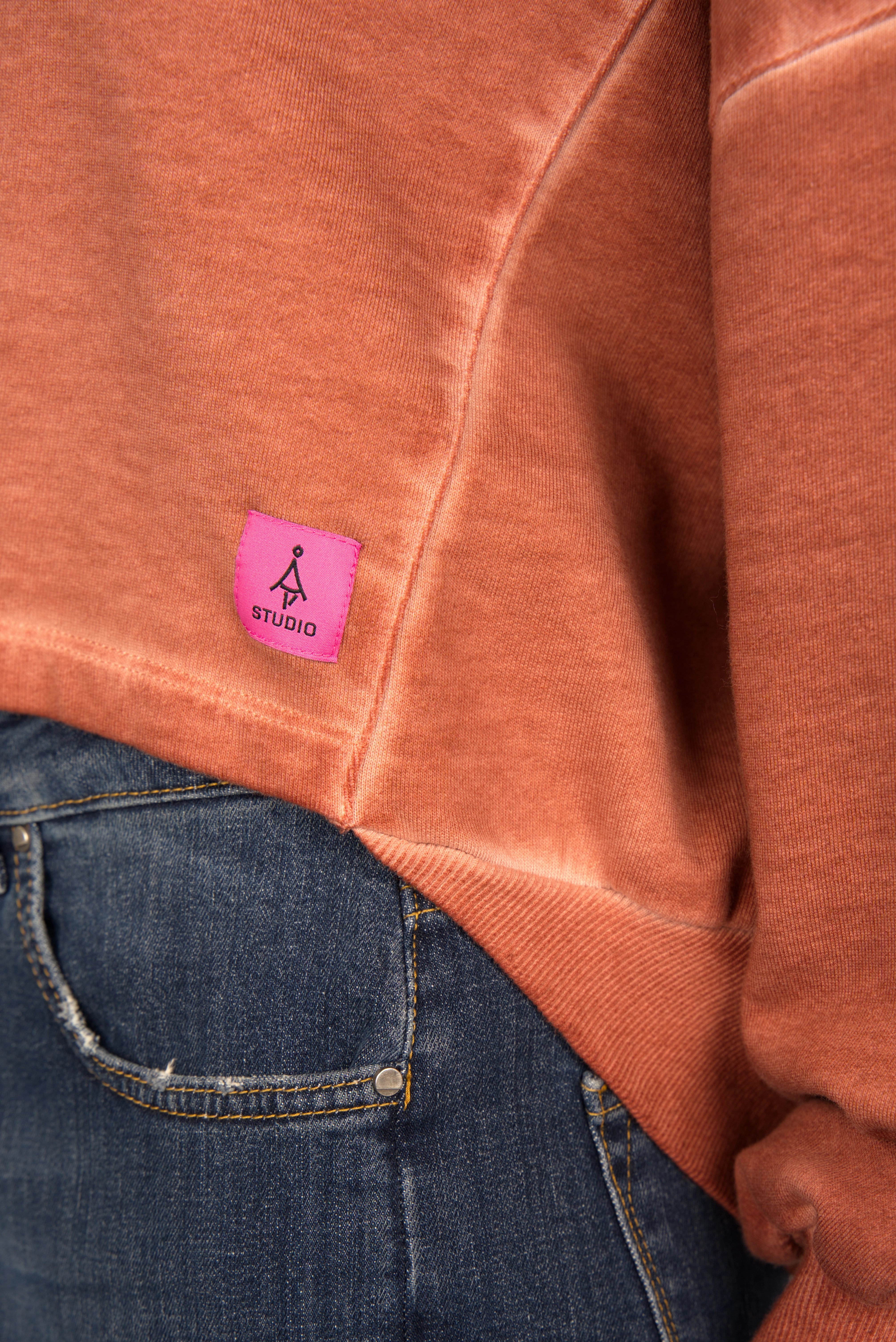 KERY Cropped Sweater with cold-washed cotton, oversized fit, U-boat neckline, pink STUDIO logo patch, and longer back hem in rust color.