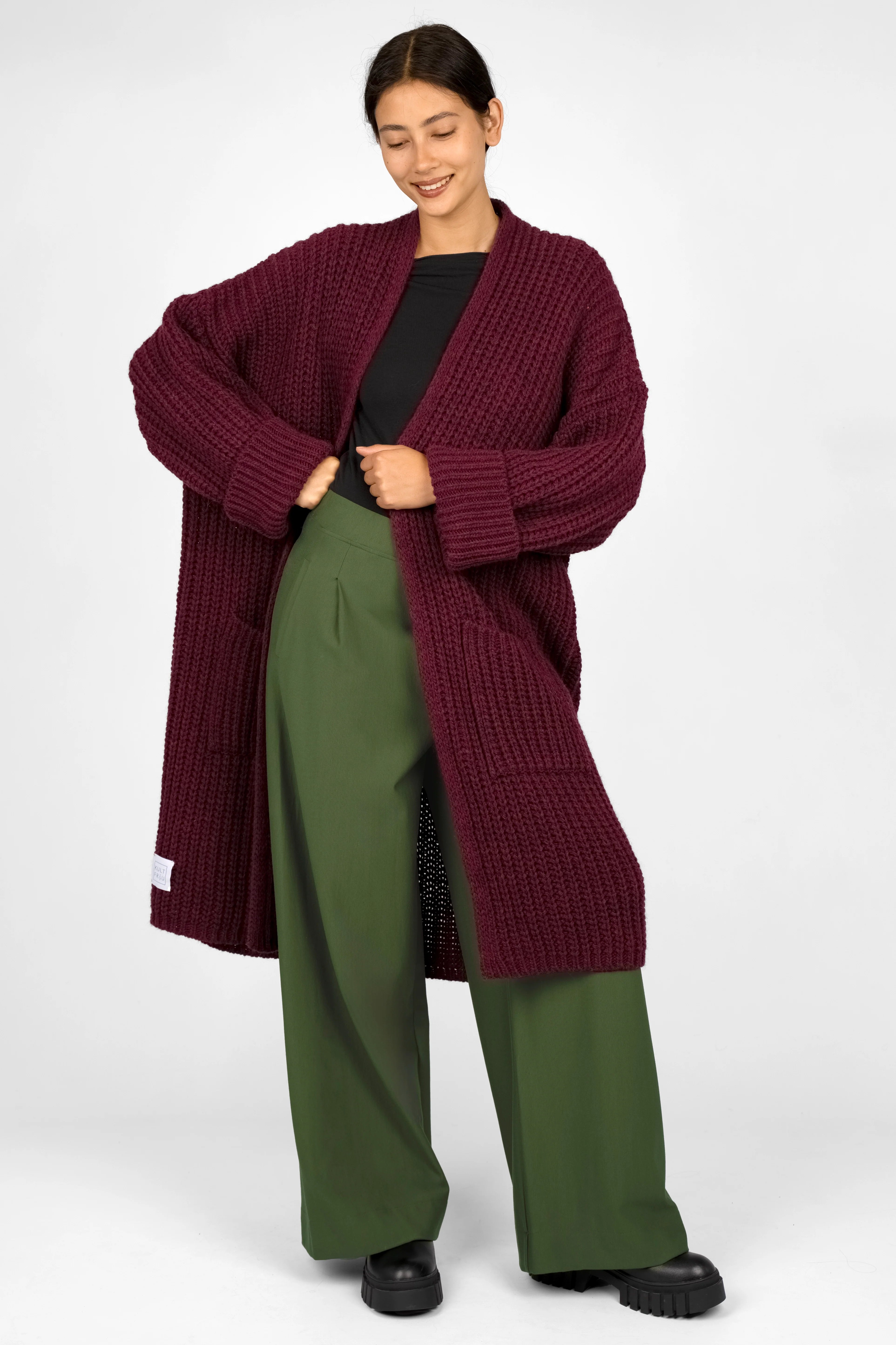 Woman wearing KLARA.K wide-leg green pants and a long burgundy knit cardigan with black shoes