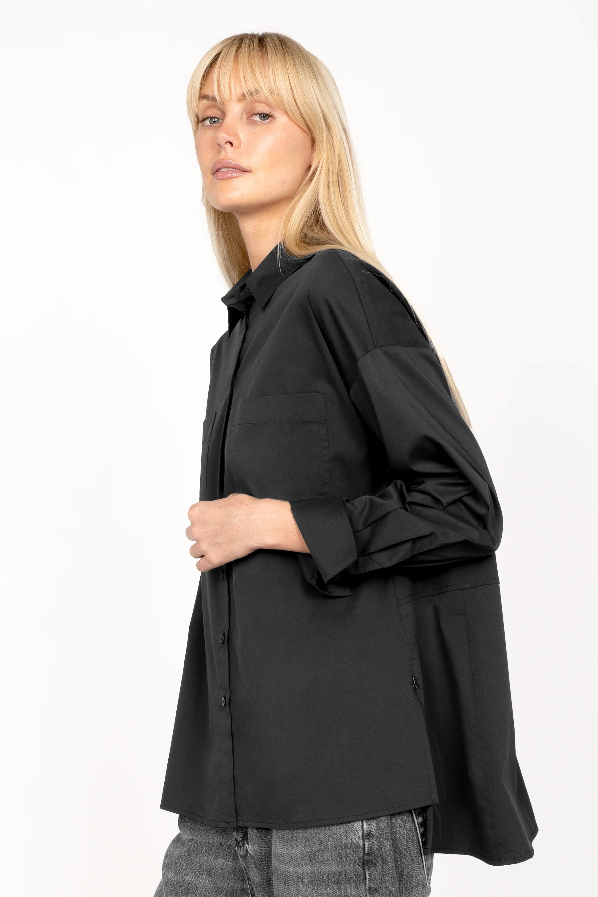Woman wearing black LEA.K Loose Fit blouse with chest pockets and wide cuffs, side slits and extended back hem.