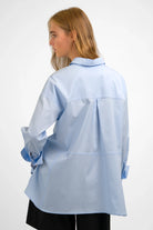 LEA.K Loose Fit light blue poplin blouse with trapezoid back and button cuffs worn by model from the back